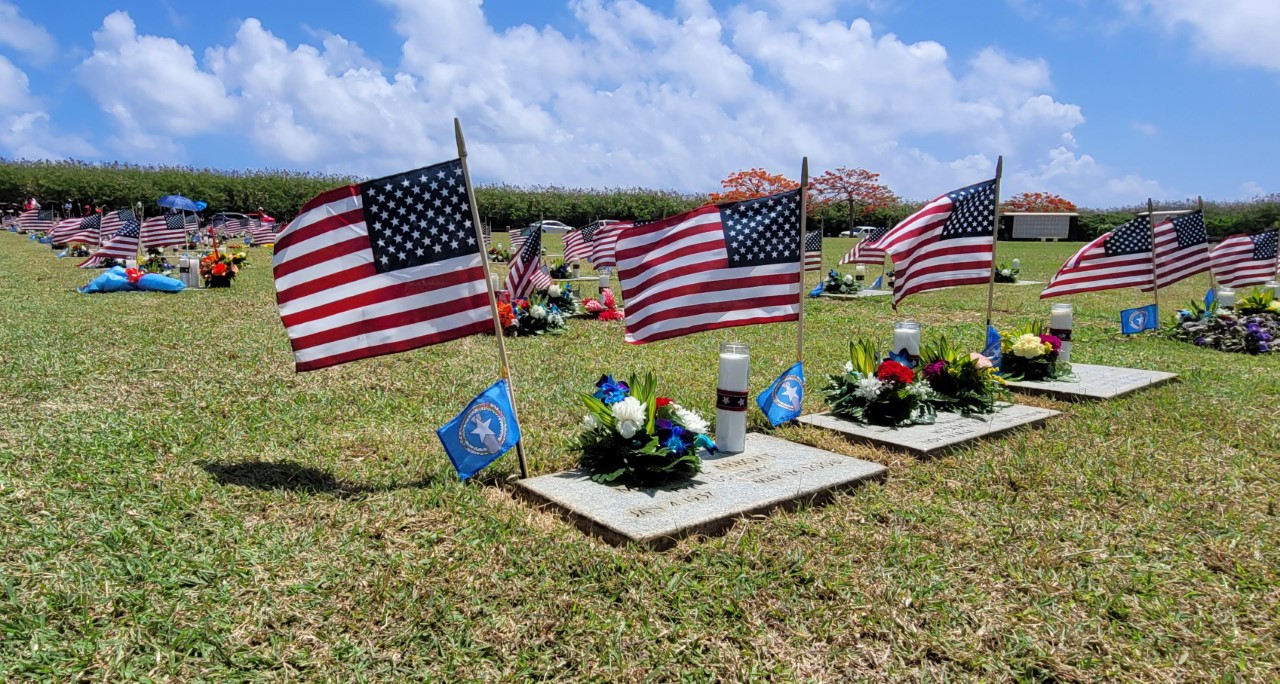 The graves at the CNMI Veterans Cemetery are  adorned with U.S. flags, CNMI flags, flowers, and a candle.