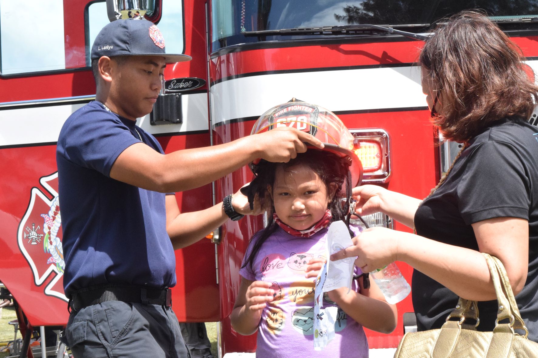 Firefighter Leo Laniyo puts his helmet on the head of eight-year-old Johana Sarabia as her mom Jeanette helps out.