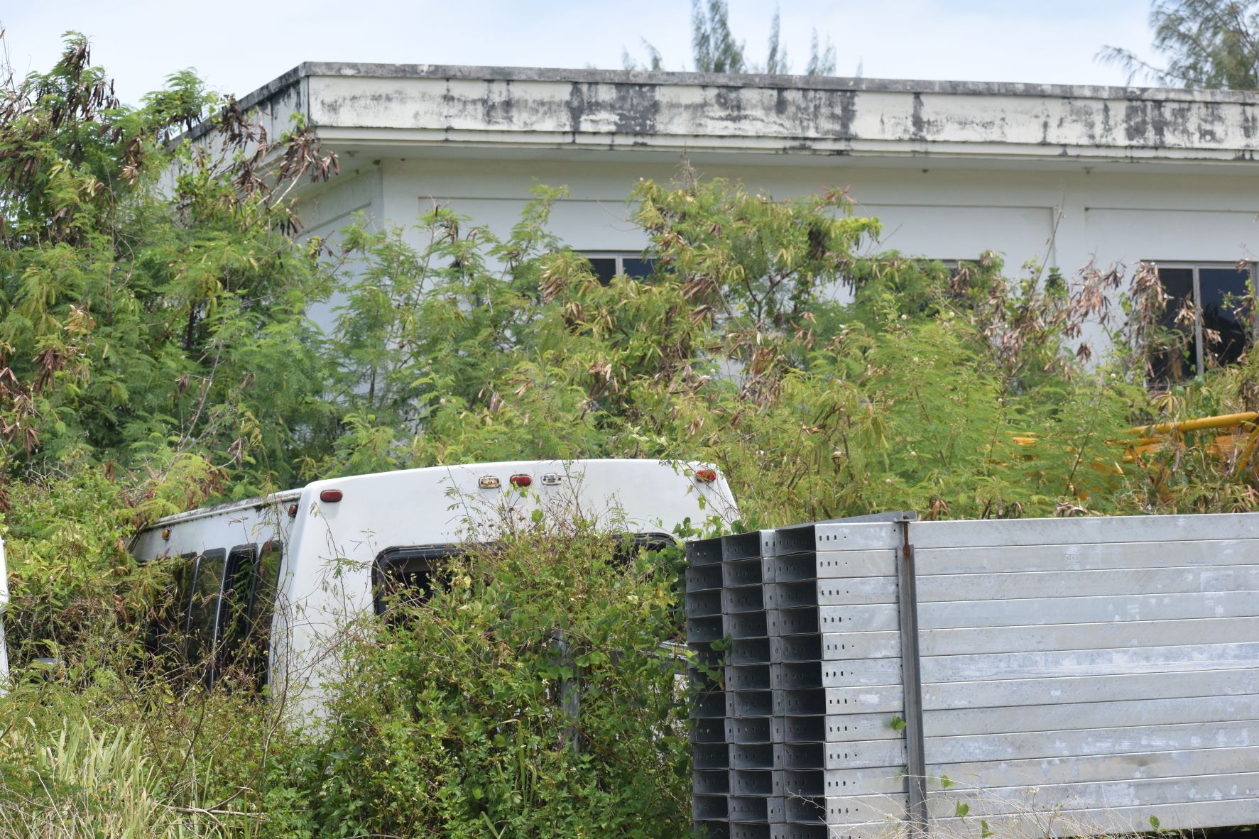 An IPI shuttle service vehicle and construction materials are surrounded by overgrown vegetation in Tanapag. Behind the building are eight barrels of used oil, according to former IPI construction team manager Jess Aquiningoc.