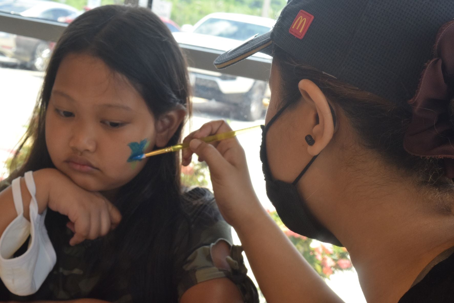 McDonald's service crewmember Gracelyn Babauta paints a butterfly on Johana Sarabia's face.
