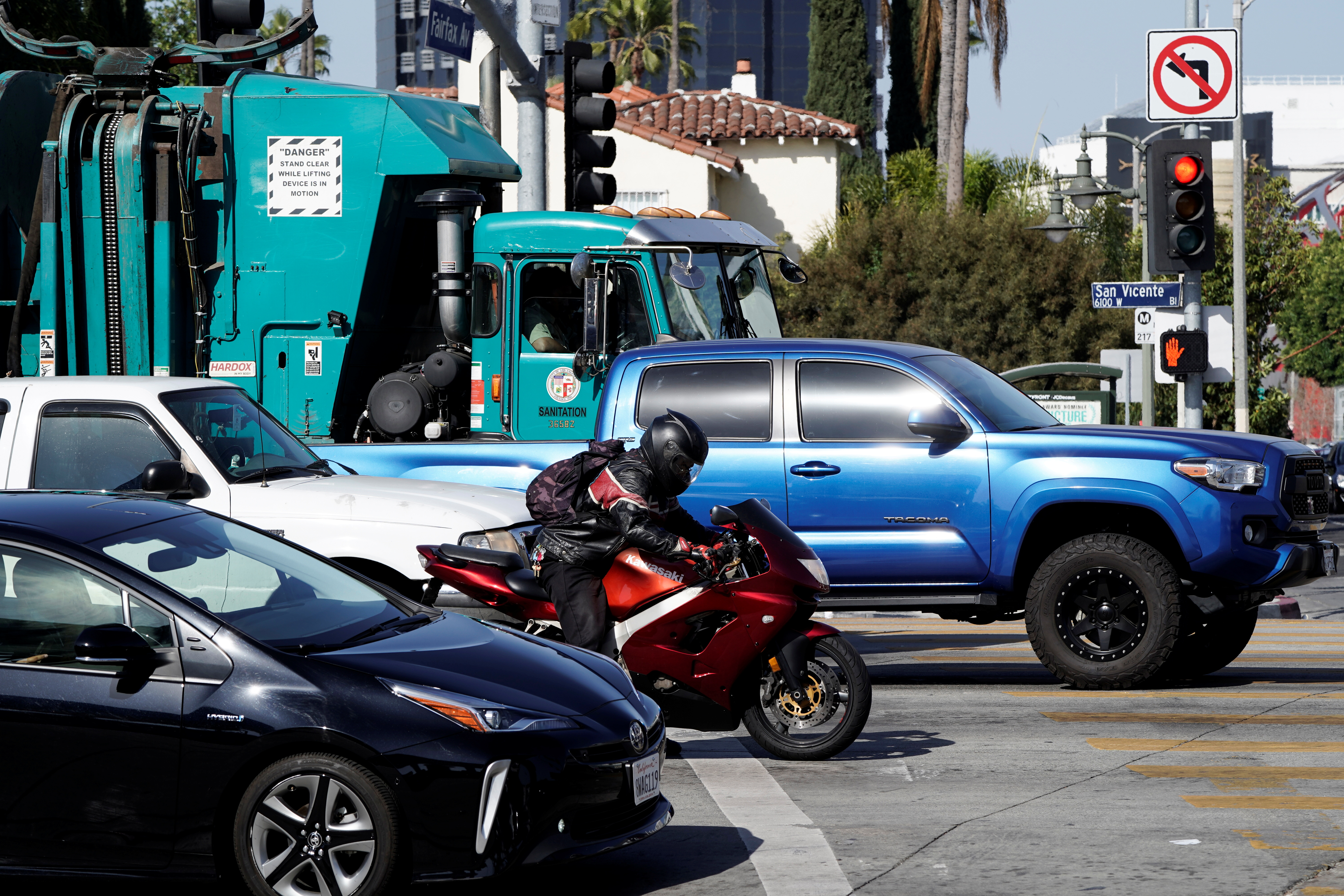 A motorcyclist waits at a red light along a car, pickup trucks and a garbage truck in Los Angeles, California, March 10, 2022.