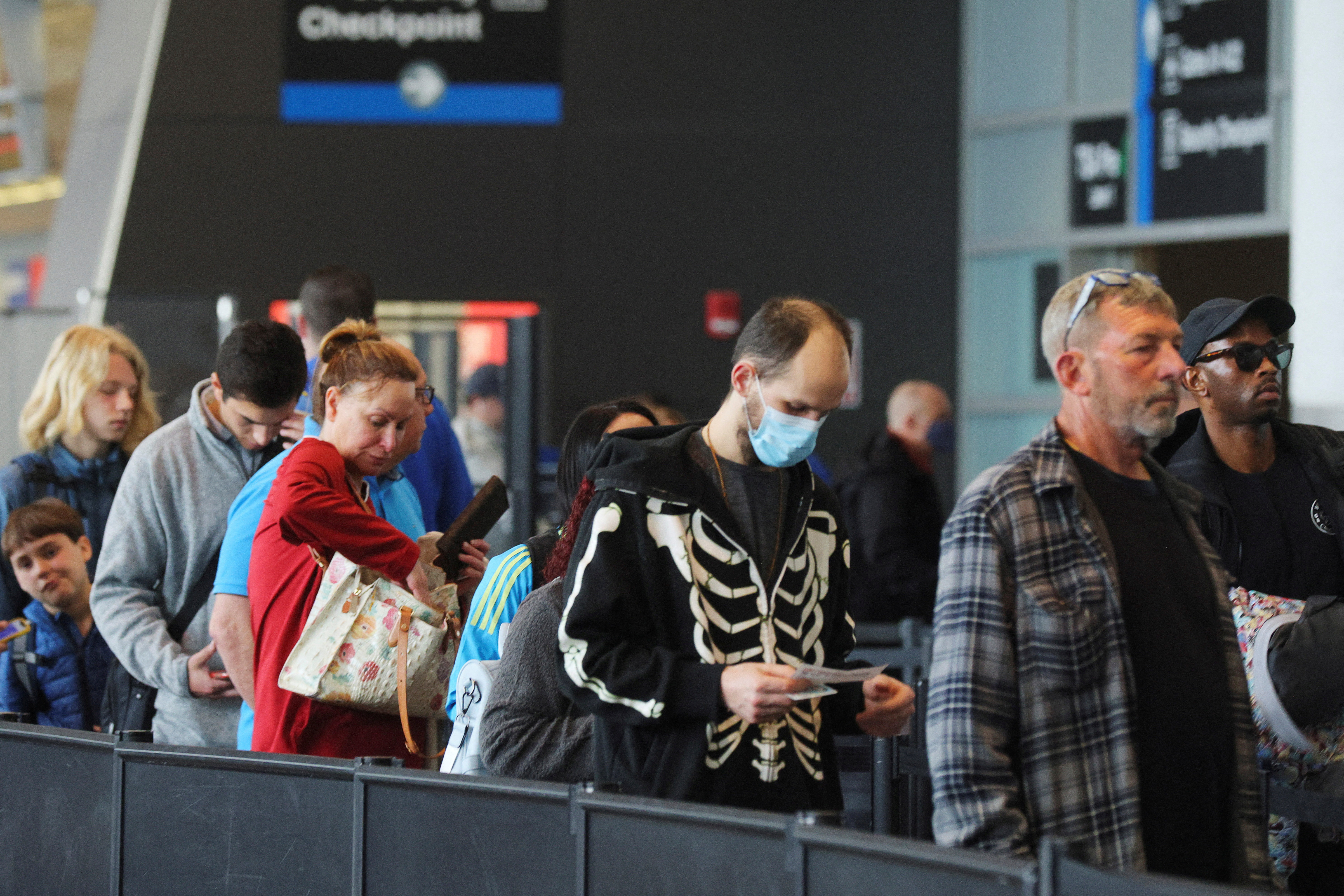 Travelers wearing masks and not wearing masks wait in line at a security checkpoint at Logan International Airport in Boston, Massachusetts, April 19, 2022.