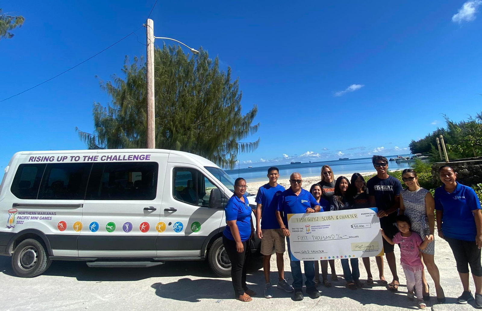 Fishguyz Scuba Charter owner and operator Sydney Takahashi and Northern Marianas Pacific Mini Games 2022 CEO Ben Babauta hold a ceremonial check for $50,000 as they pose for a photo with Fishguyz staff  and Pacific Games Council members Thursday, June 2, at  Sugar Dock.