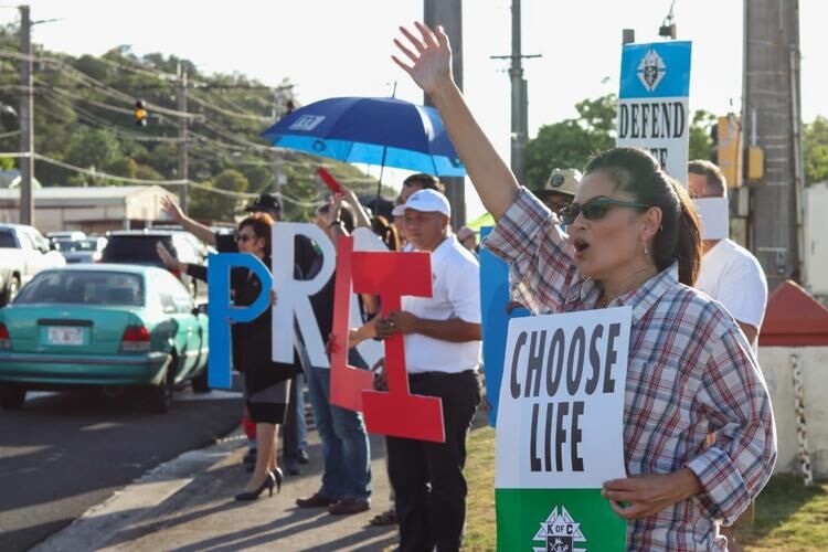 Michelle Armenta, right, with the Catholic Pro-Life Committee, waves to passing motorists during an anti-abortion prayer rally on Route 1 in Adelup, Guam in June 2019.