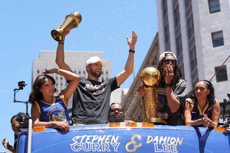Golden State Warriors guard Stephen Curry gestures while standing with wife Ayesha, far left, and guard Damion Lee, center right, and his wife Sydel Curry, far right,  during the Golden State Warriors championship parade in downtown San Francisco on June 20, 2022.