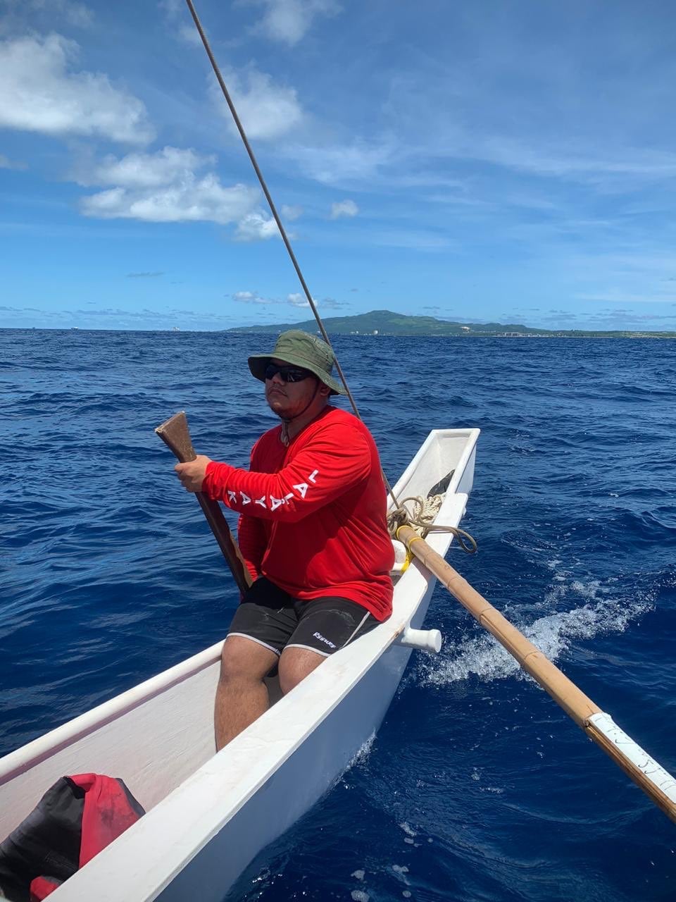 Andrew Roberto, under the guidance of Master Navigator Cecilio Raiukiulipiy — not pictured — uses a poksai to steer Neni across the Saipan-Tinian Channel. Saipan is pictured in the background.