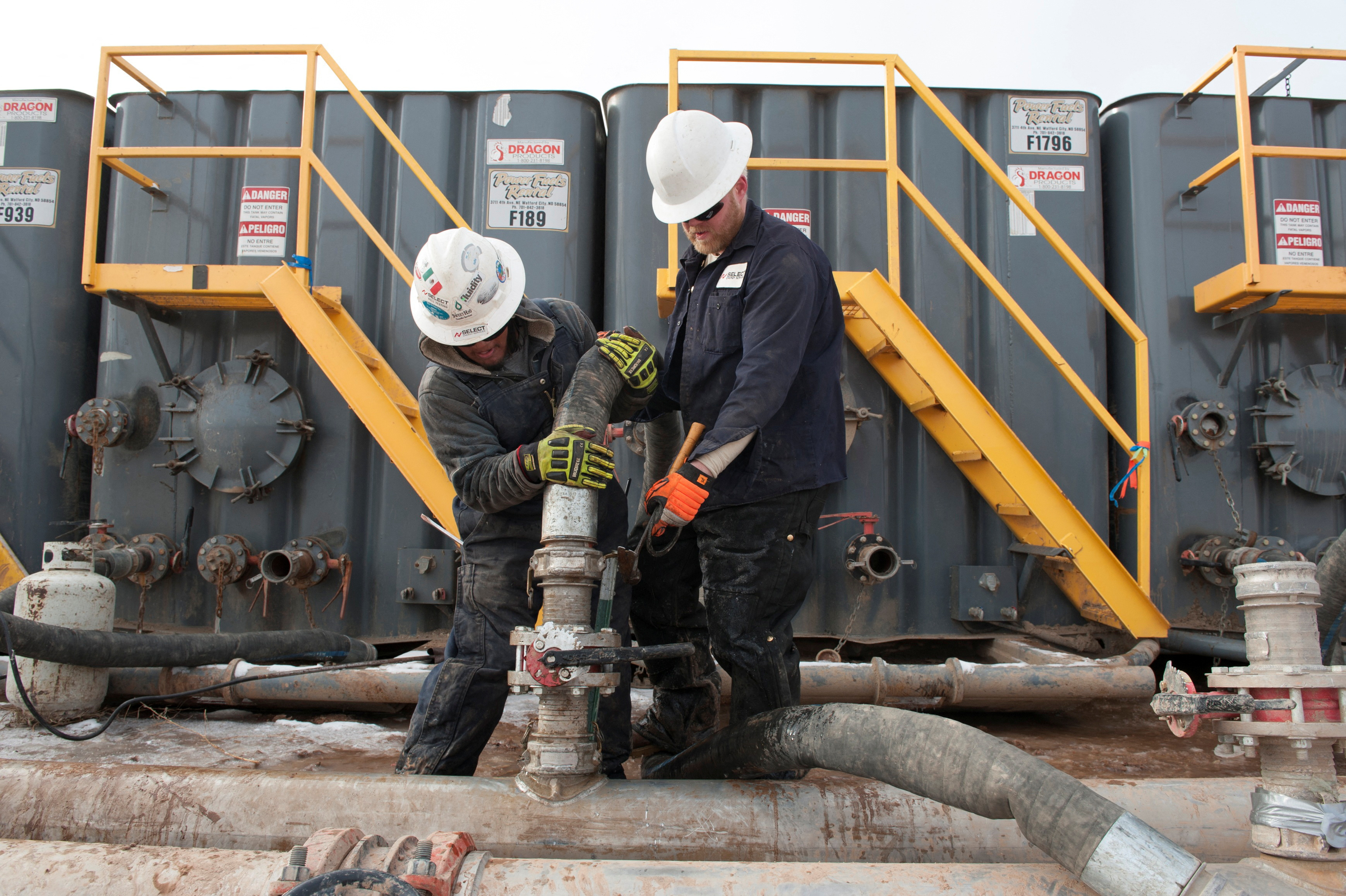 Workers connect hoses between a pipeline and water tanks at a Hess fracking site near Williston, North Dakota on Nov. 12, 2014.