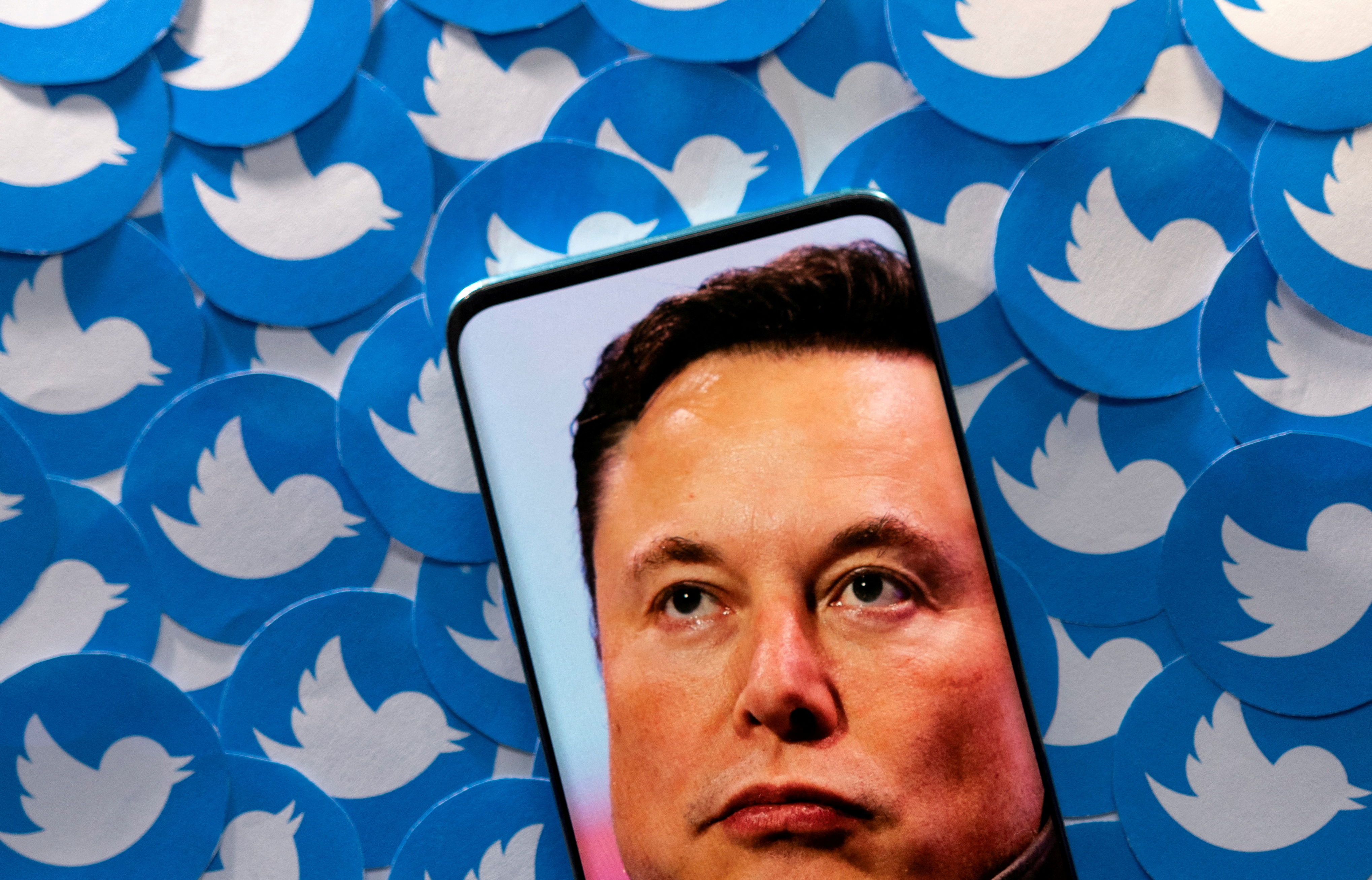 An image of Elon Musk is seen on smartphone placed on printed Twitter logos in this picture illustration taken April 28, 2022.