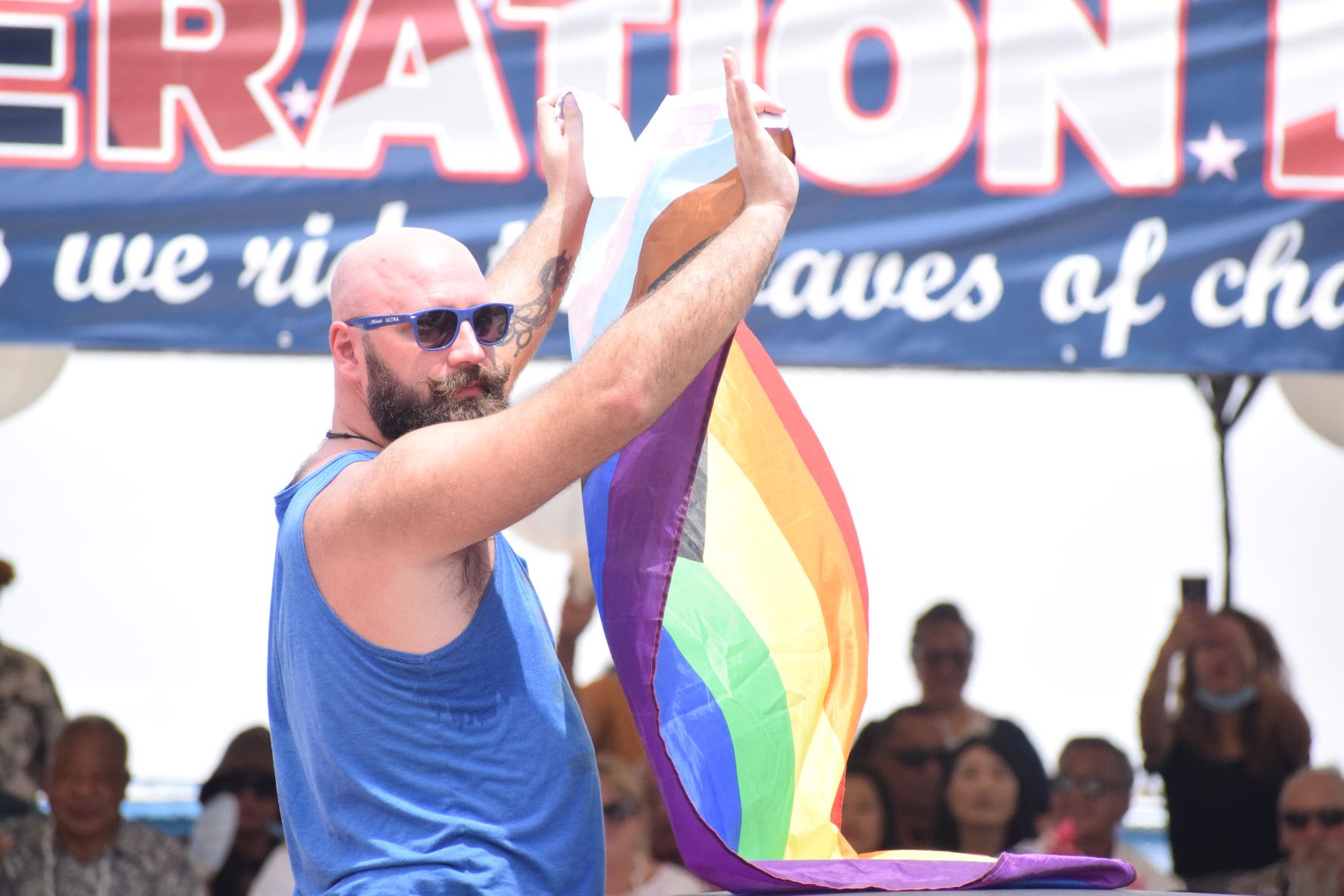 An LGBTQ+ advocate displays a rainbow flag as he rides on the float representing PRIDE Marianas.