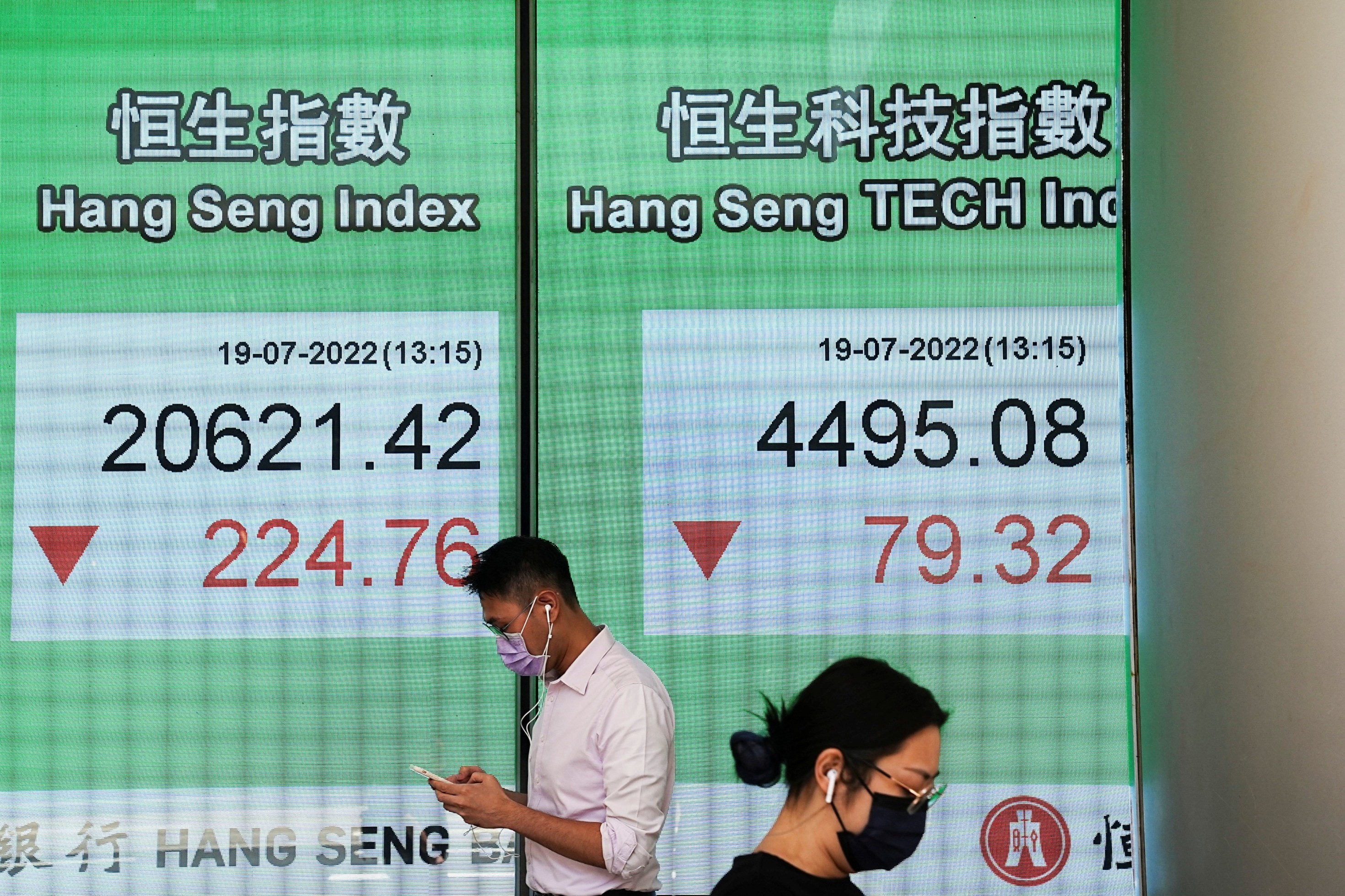 People walk past a screen displaying the Hang Seng stock index at Central district, in Hong Kong, China, July 19, 2022.