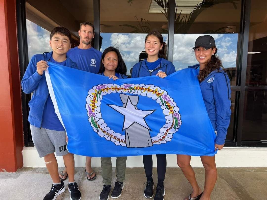 Taiyo Akimaru, Coach Richard Sikkel, Maria Batallones, Jinie Thompson and Coach Ally Pourmonir pose with the CNMI flag before heading out to compete in the 19th FINA World Championships in Budapest, Hungary.