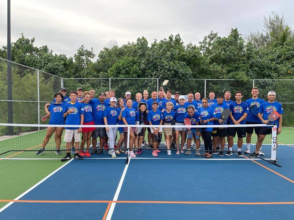 Participants pose for a photo before the start of the inaugural pickleball event at the newly striped court at American Memorial Park on Saturday.