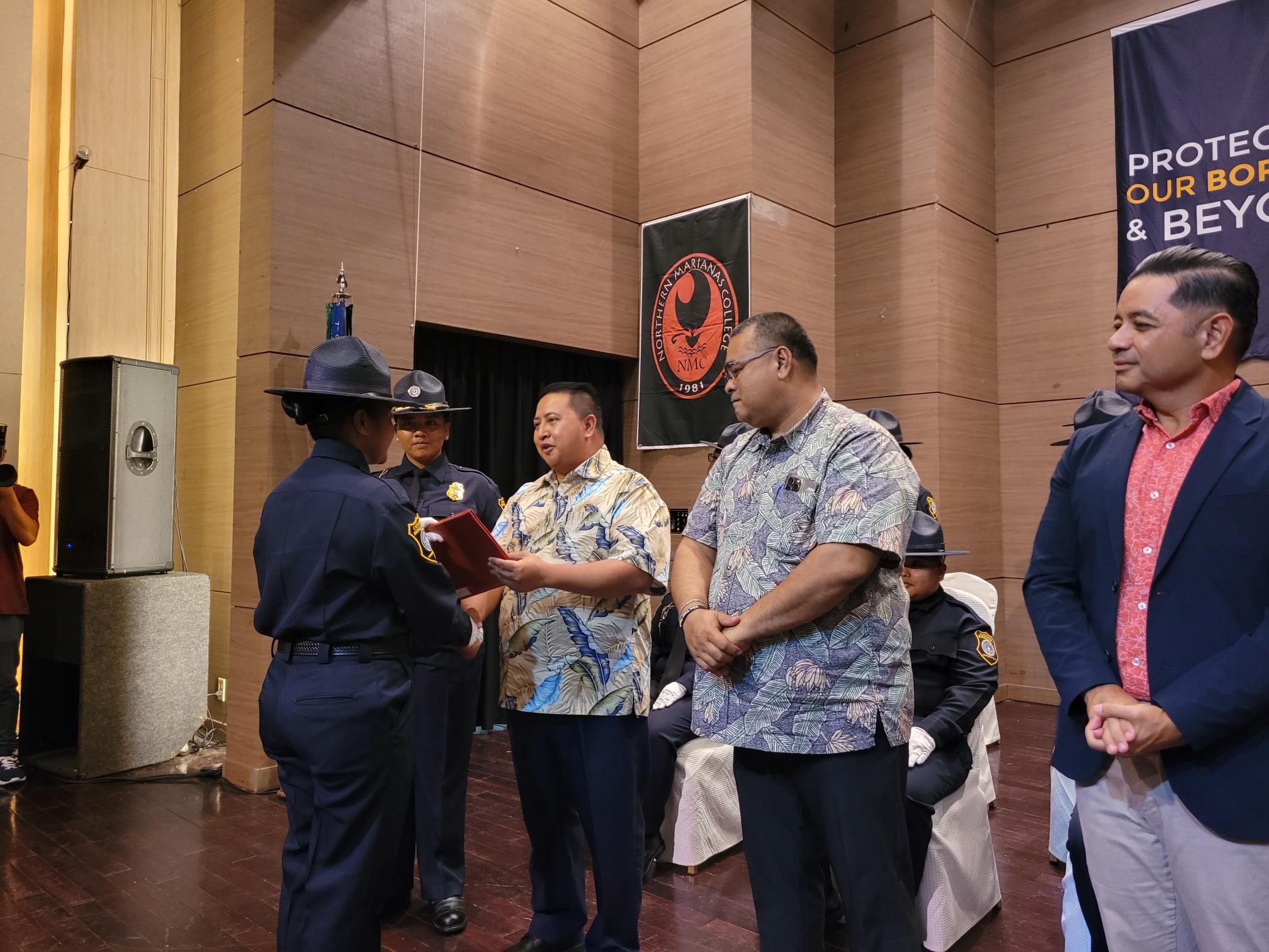 9th Cycle Customs and Biosecurity Academy valedictorian Uchelbil E. Oiterong is congratulated by Gov. Ralph DLG Torres while Department of Finance Secretary David Atalig looks on.