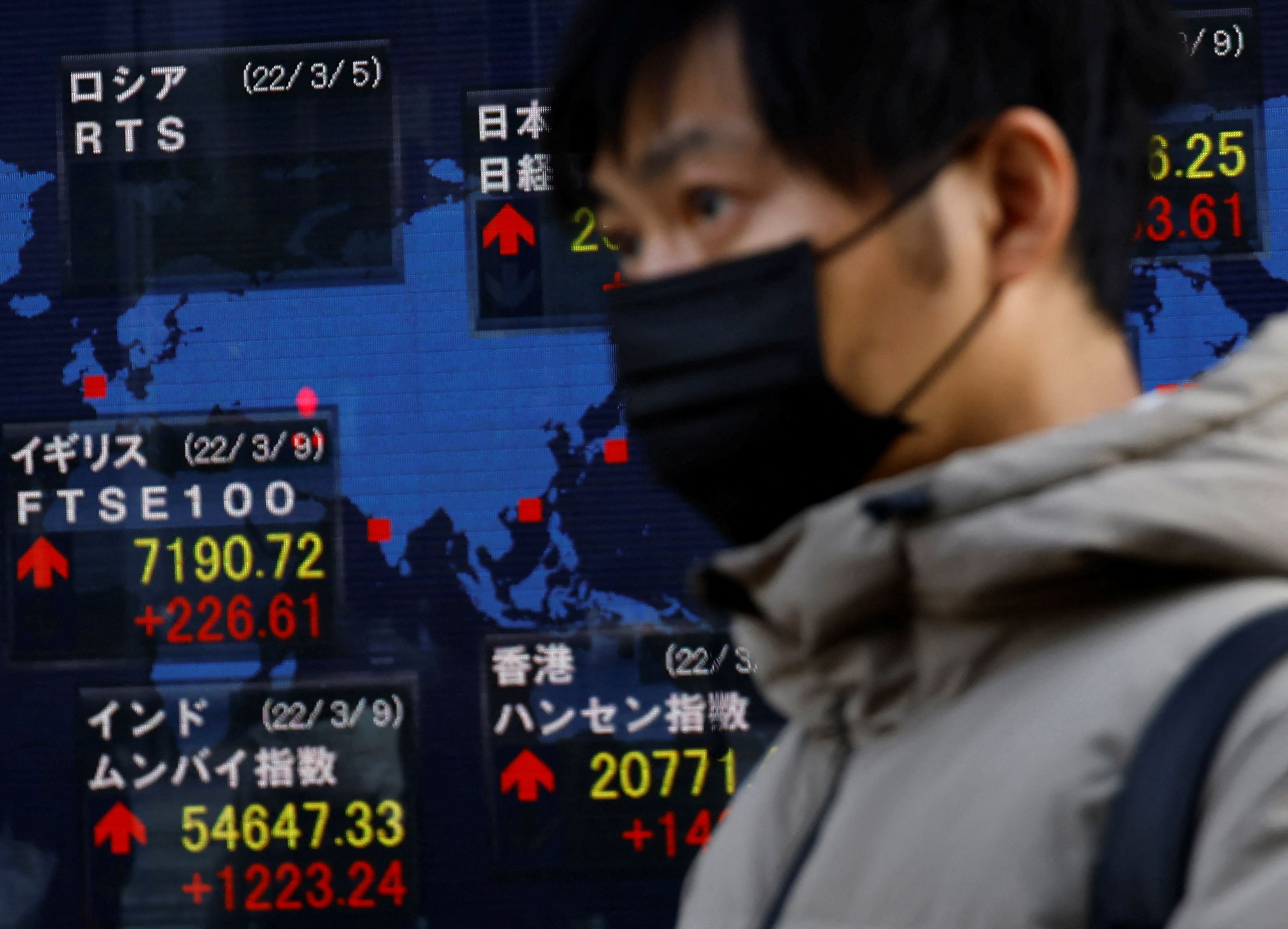 A man wearing a protective mask walks past an electronic board displaying various countries' stock indexes including the Russian Trading System Index, which is empty, outside a brokerage in Tokyo, Japan, March 10, 2022.