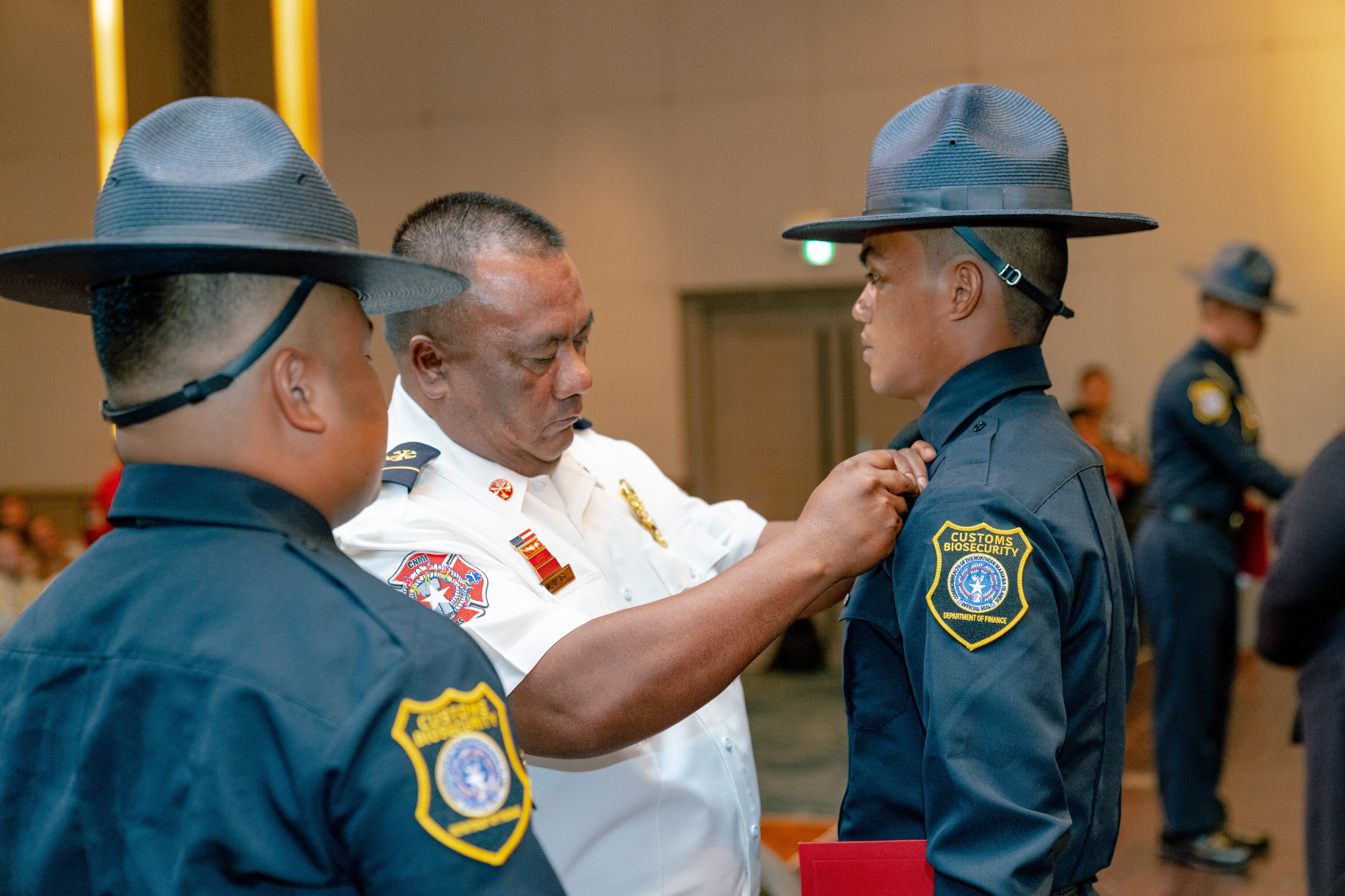 Division of Customs and Biosecurity 9th Cycle Academy graduate Aurel Mendiola receives his badge from his uncle, Fire Chief John Blas, as Academy Drill Instructor Mark Manaluz looks on.