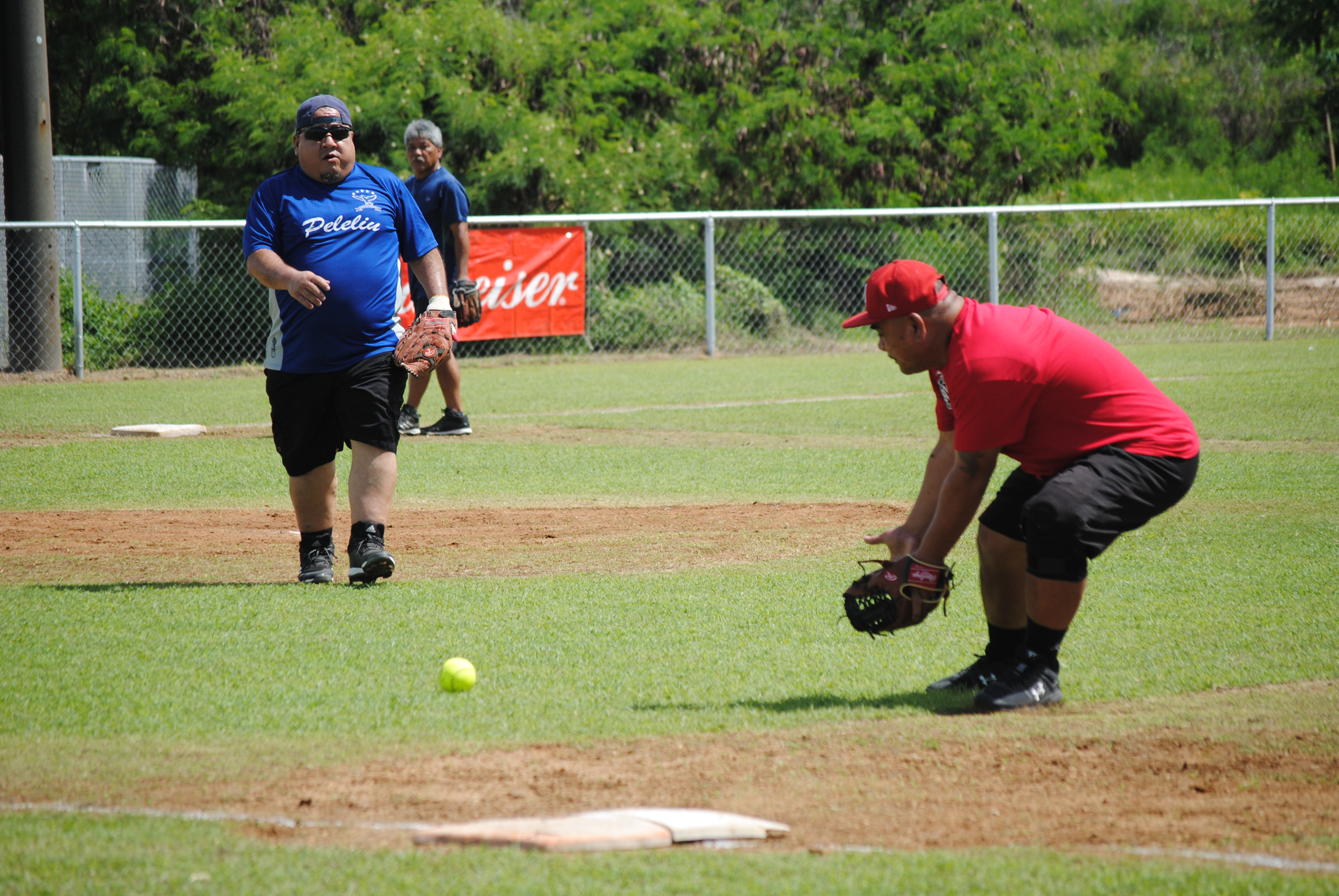 Peliliu's first baseman Jun bends to catch the grounder as pitcher Ray looks on.