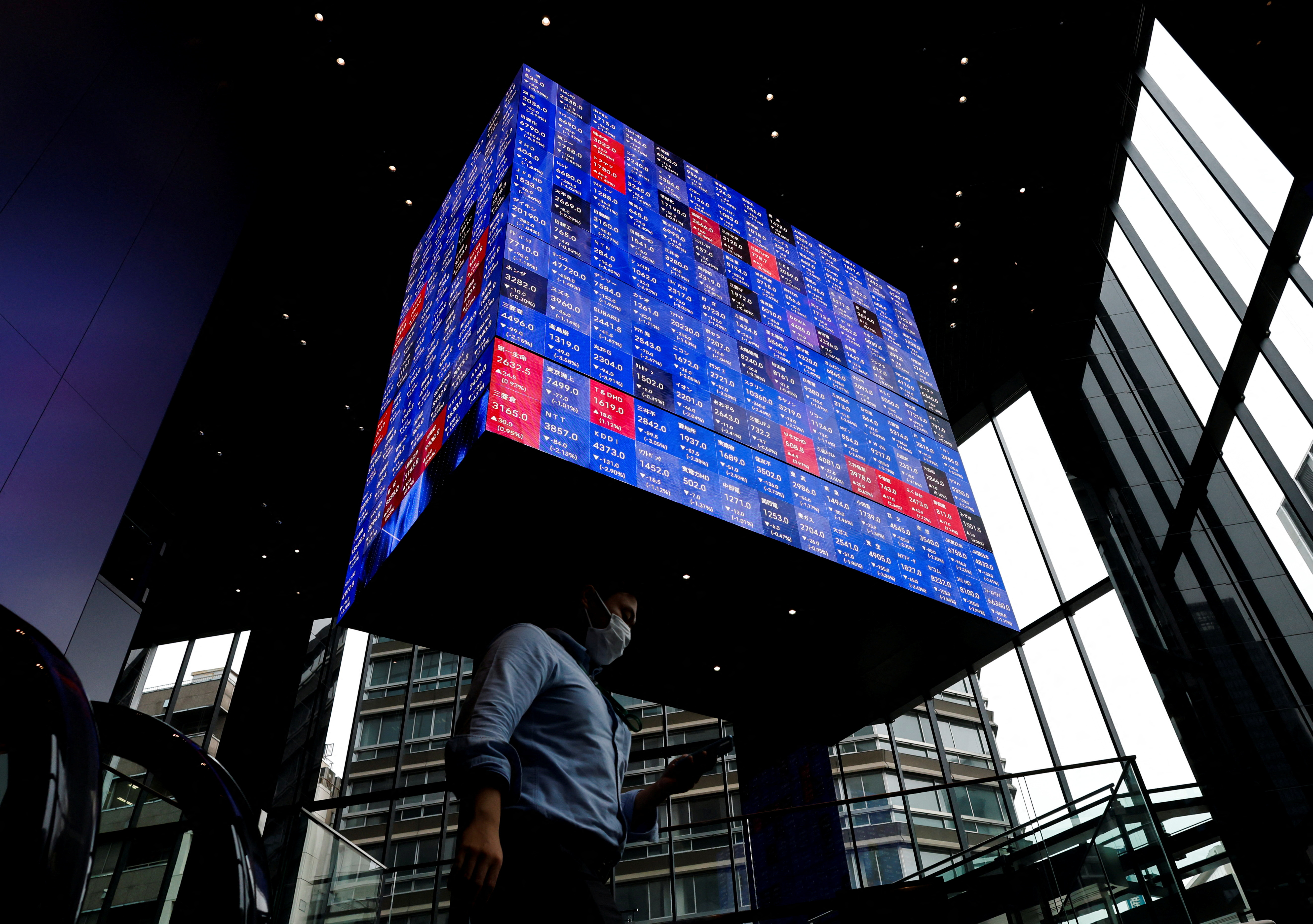 A man walks under an electronic screen showing Japan's Nikkei share price index inside a conference hall in Tokyo, Japan on June 14, 2022.