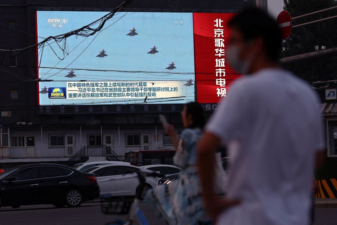 Pedestrians wait at an intersection near a screen showing footage of Chinese People's Liberation Army aircraft during an evening news program in Beijing, China Aug. 2, 2022.
