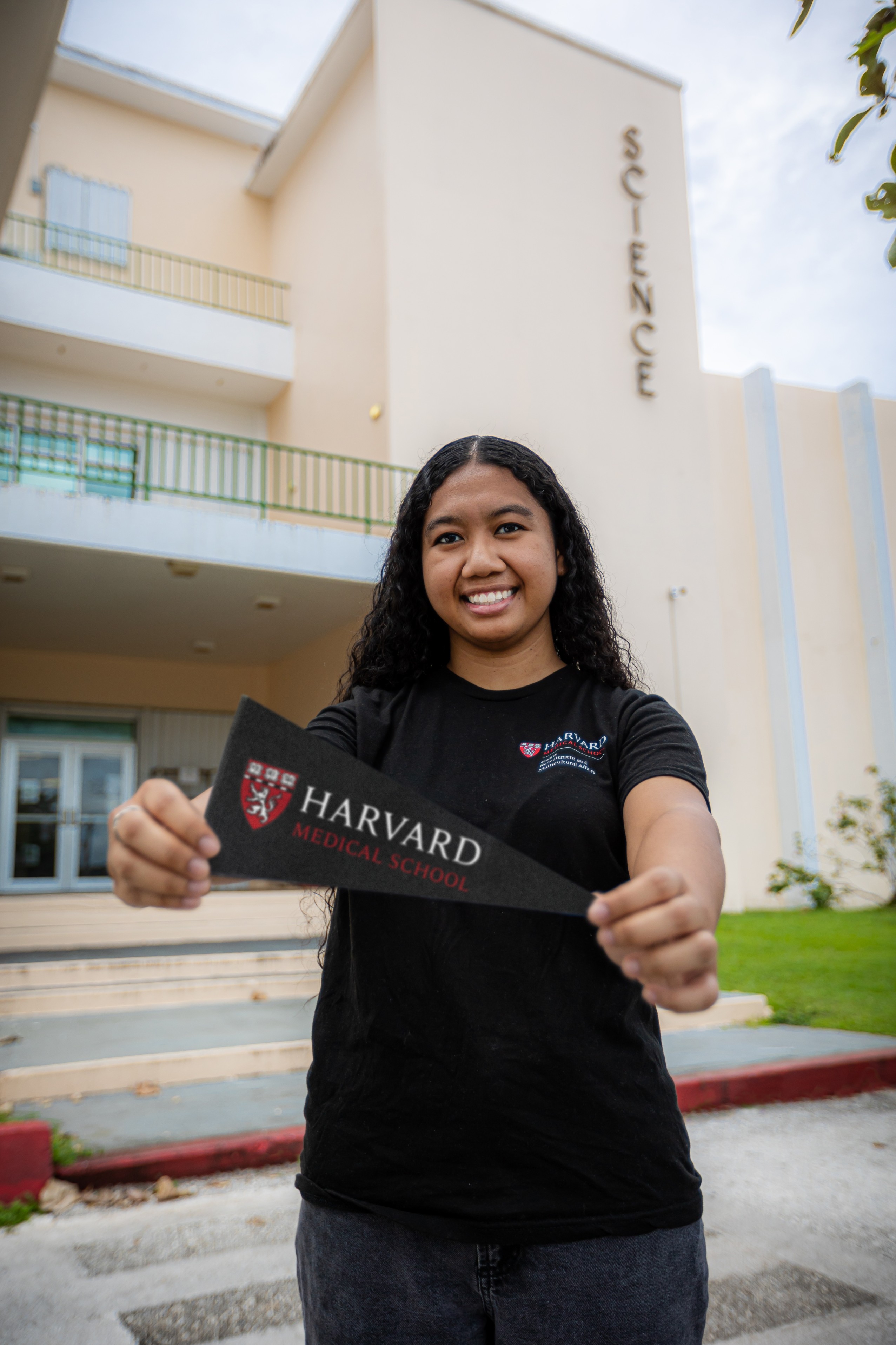 Megan Gimmen stands outside the Science Building on the University of Guam campus holding the Harvard Medical School pennant, where she began a Doctor of Medicine program on a full scholarship on Aug. 1. She graduated as valedictorian from both Okkodo High School in 2016 and the University of Guam in 2020, where she double majored in biology and chemistry.