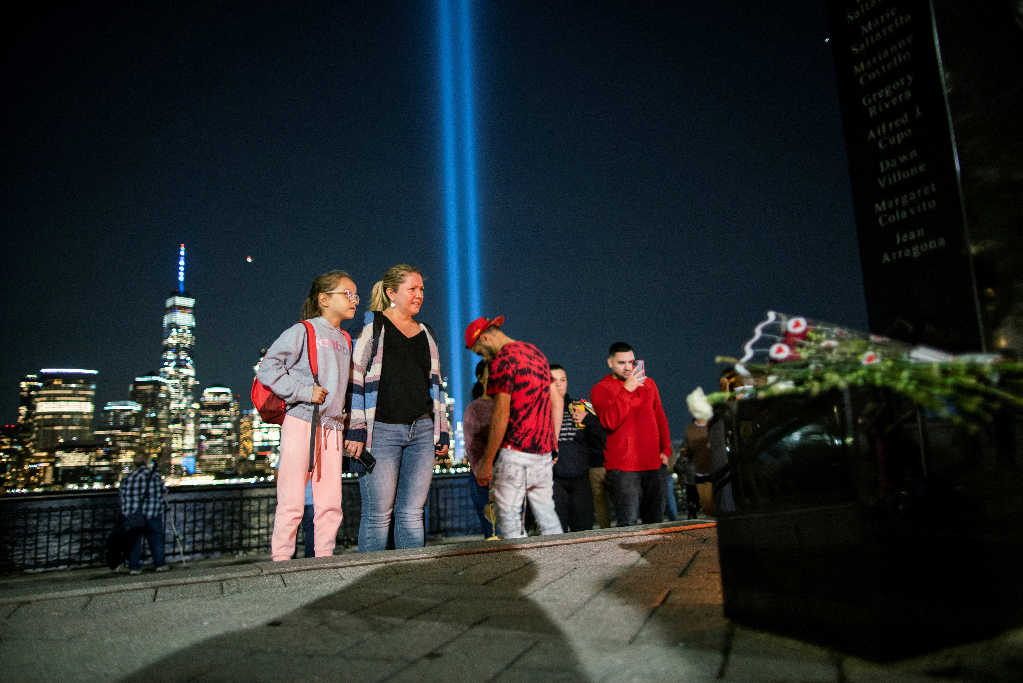 People pay respect for the victims at a memorial while the Tribute in Light art installation and the One World Trade Center are seen in the background on the 20th anniversary of the Sept. 11, 2001 attacks in New York City, as it is seen from Exchange Place, New Jersey, Sept. 11, 2021.