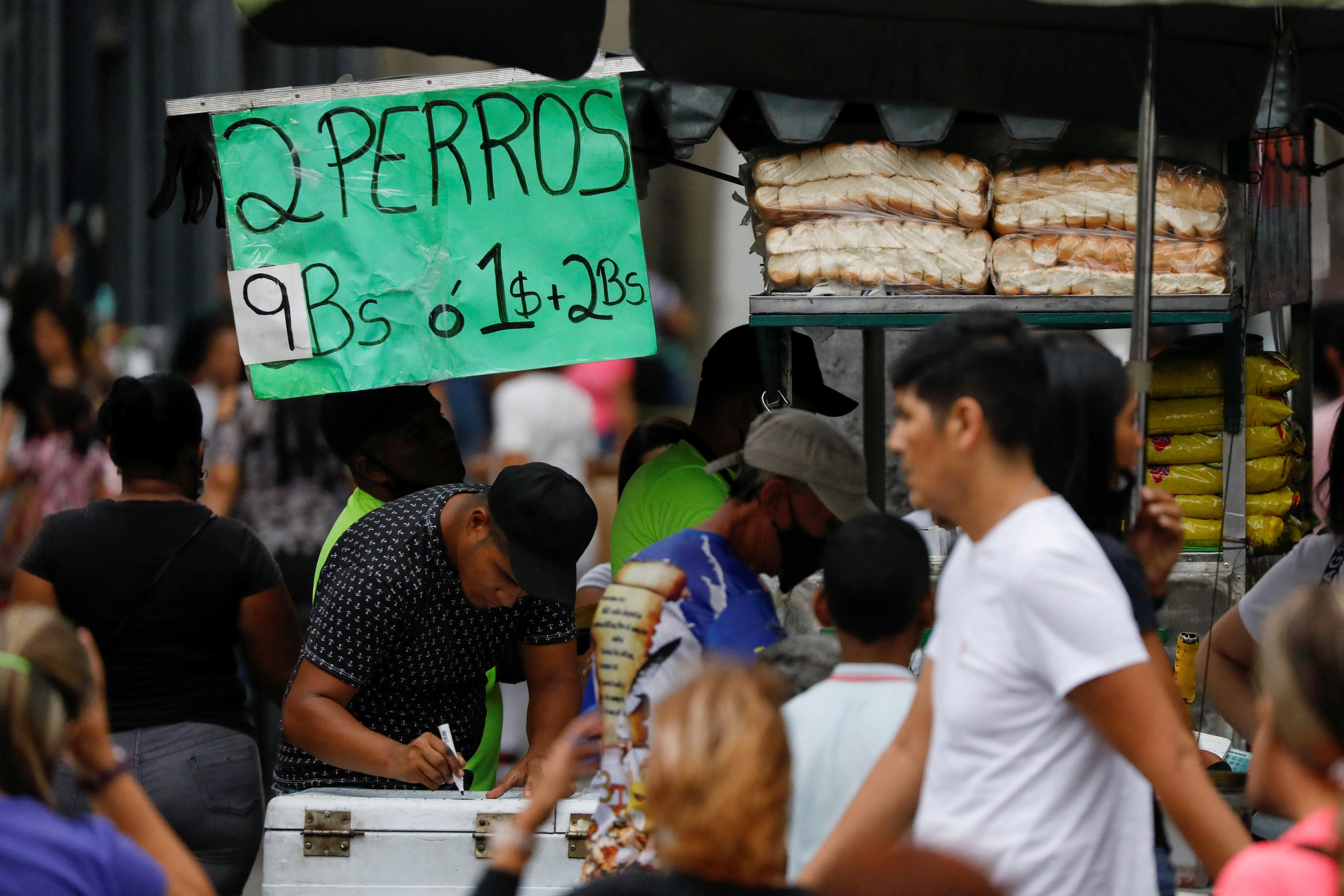 People walk past a hot dog stand with a sign reading "Two hot dogs for 9 Bolivars, or 1 U.S. dollar + 2 Bolivars," in Caracas, Venezuela, Aug. 25, 2022.