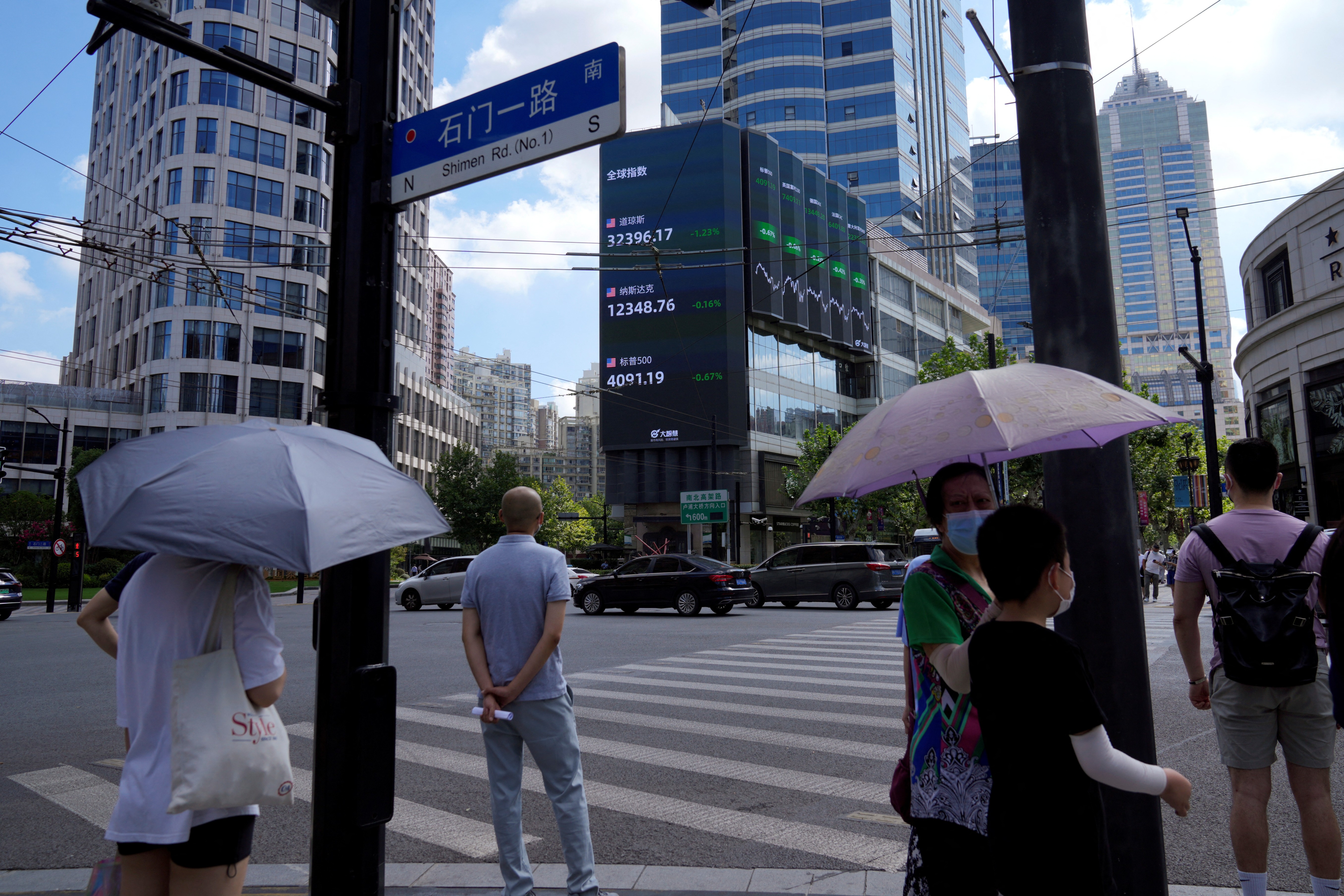 Pedestrians wait to cross a road at a junction near a giant display of stock indexes in Shanghai, China, Aug. 3, 2022.