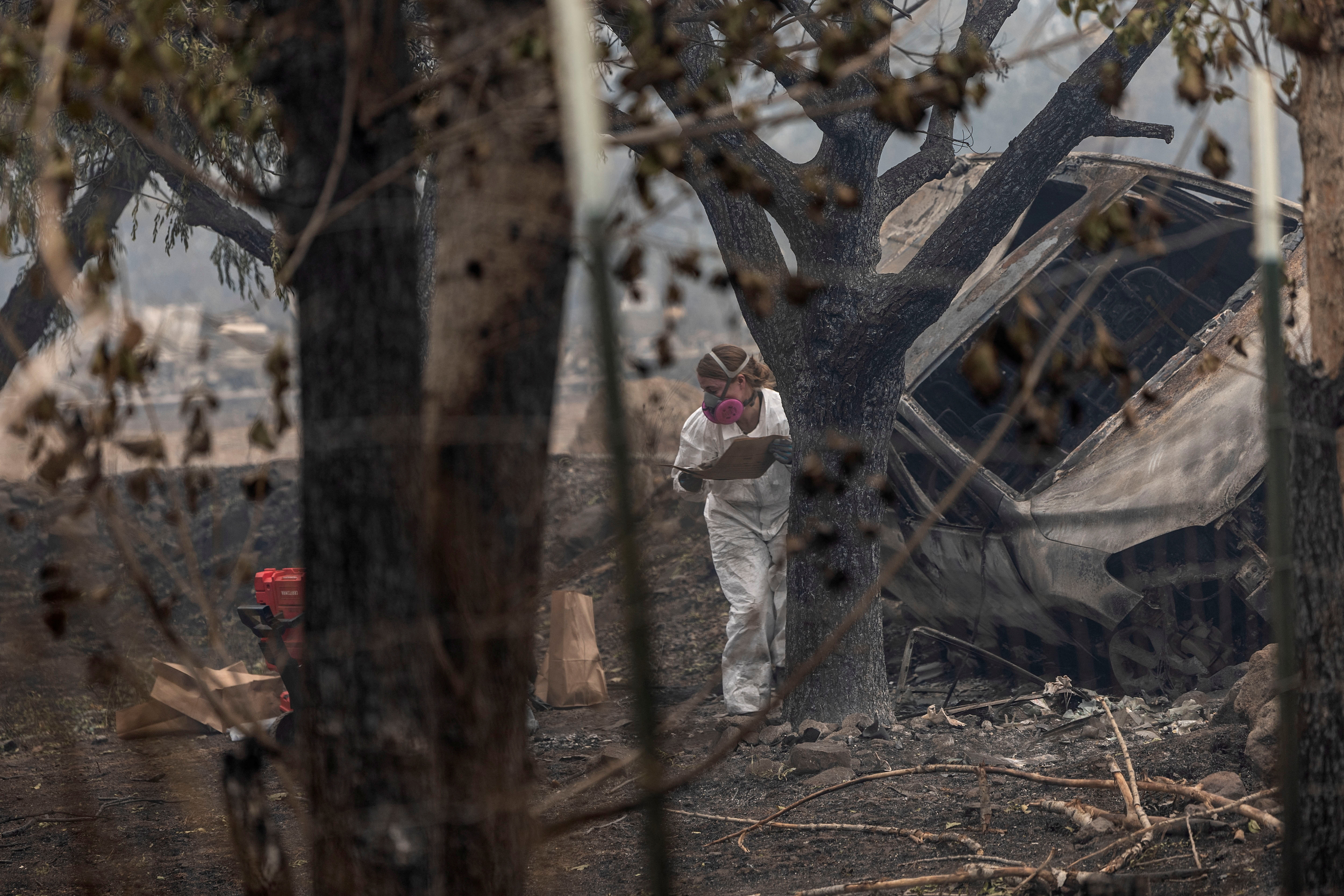 A forensic anthropologist looks for human remains in a damaged vehicle as the McKinney Fire burns near Yreka, California, Aug. 1, 2022.
