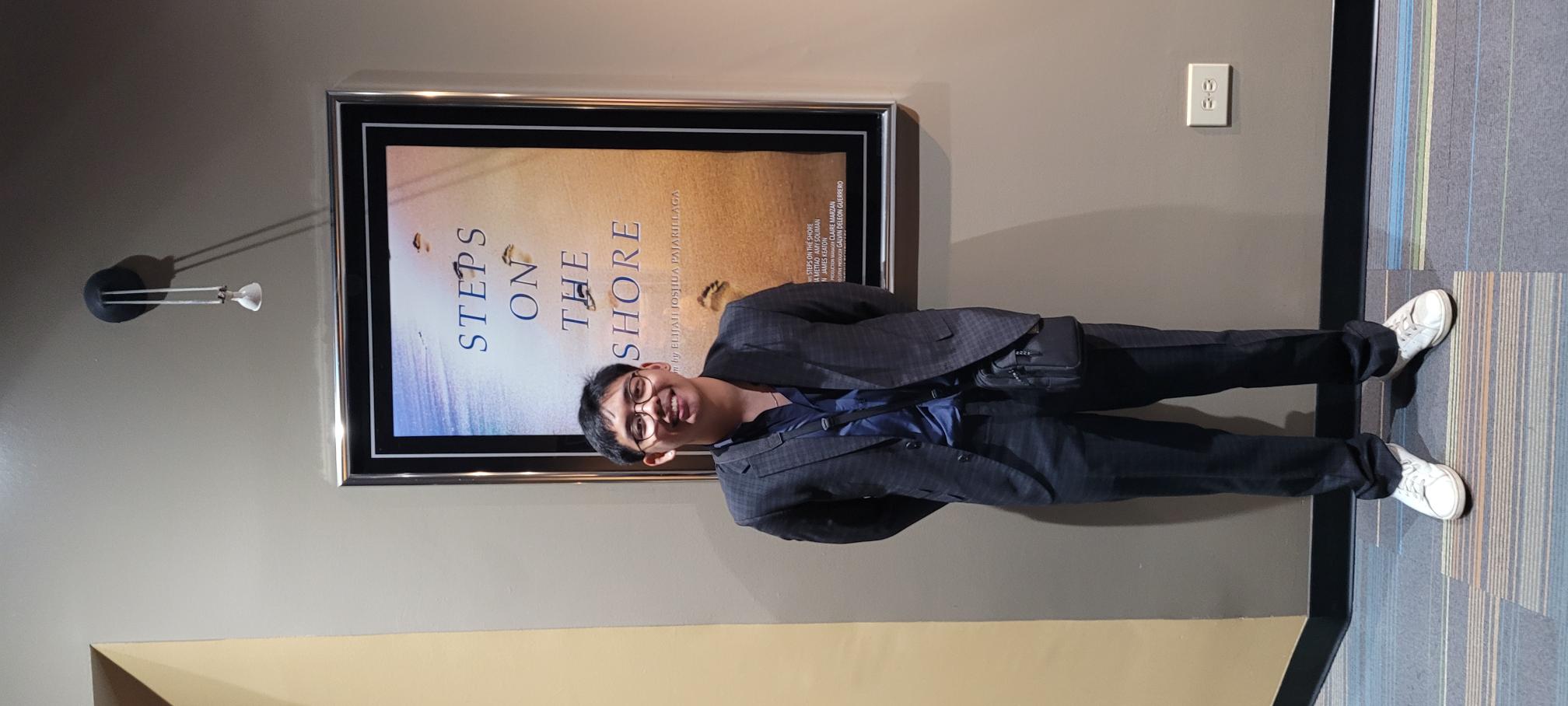 Filmmaker Elijah Joshua Pajarillaga poses for a photo in front of the poster for his new film, "Steps on the Shore," which premiered at Hollywood Theaters on Monday night.