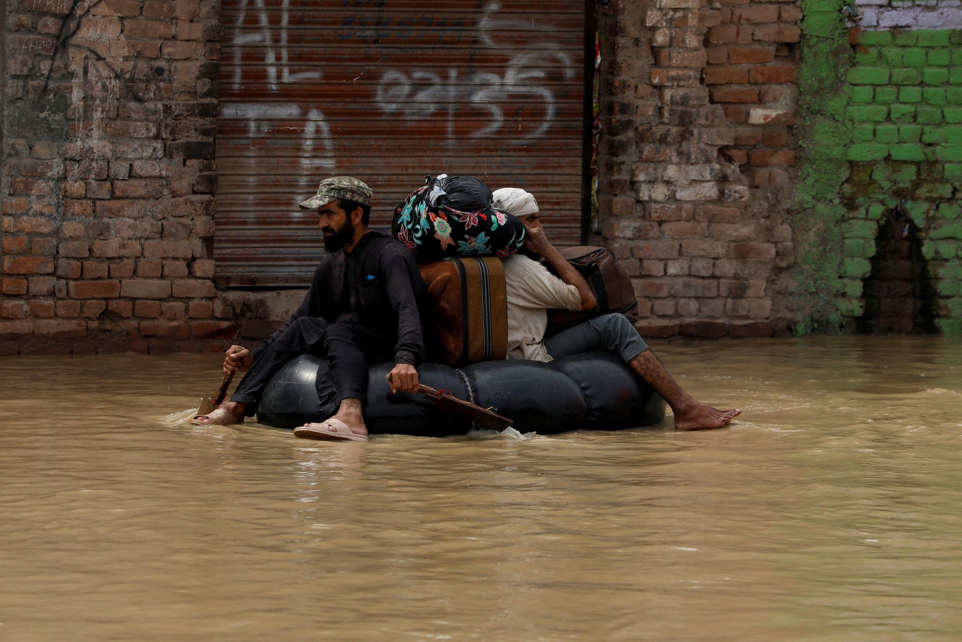 A volunteer paddles an inflatable tube as he evacuates a flood victim with his belongings, following rains and floods during the monsoon season in Charsadda, Pakistan on Aug. 27, 2022.