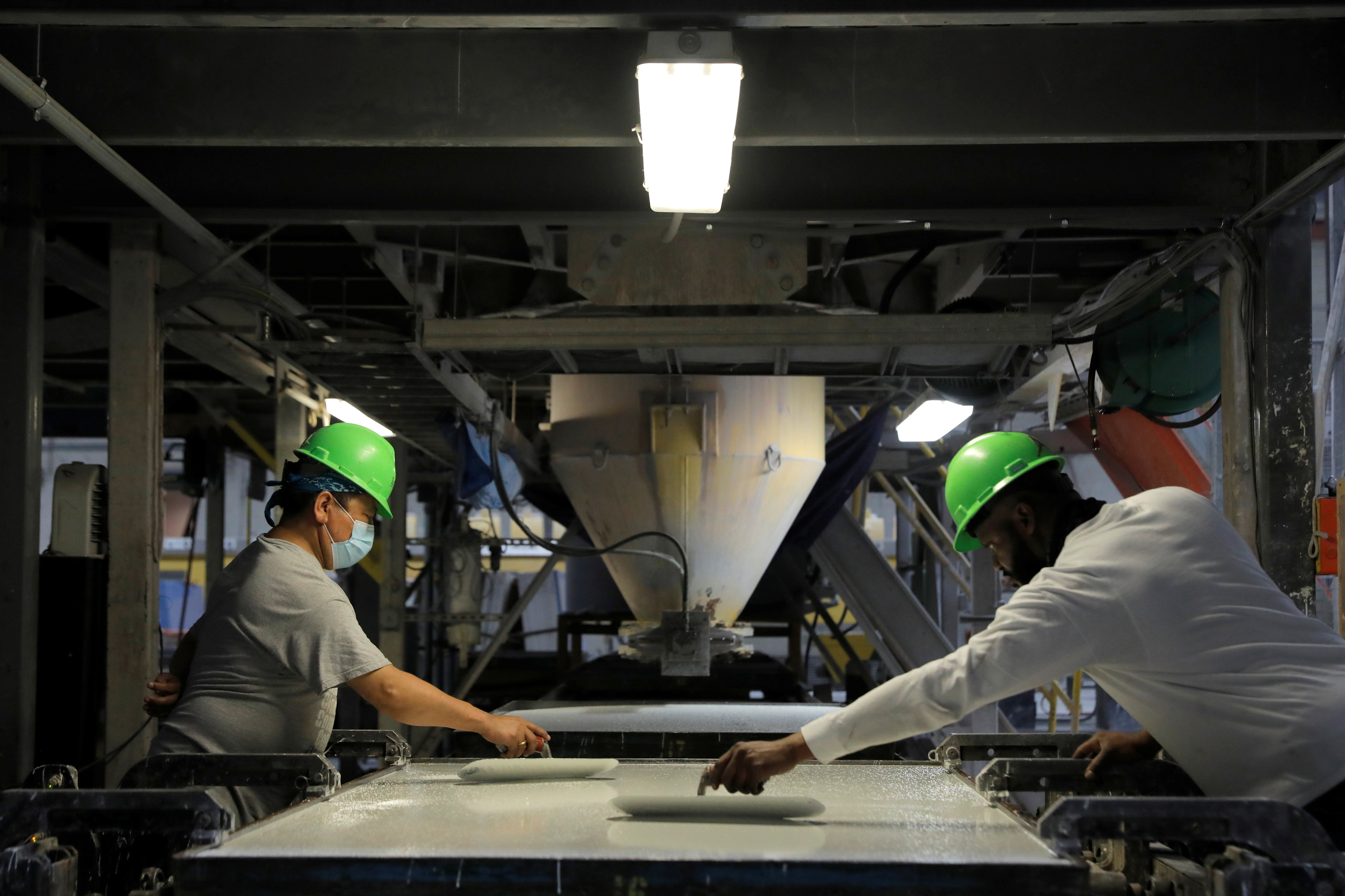 Cap:Workers trowel the poured mixture of a slab in the factory of IceStone, a manufacturer of recycled glass countertops and surfaces, in New York City, June 3, 2021.