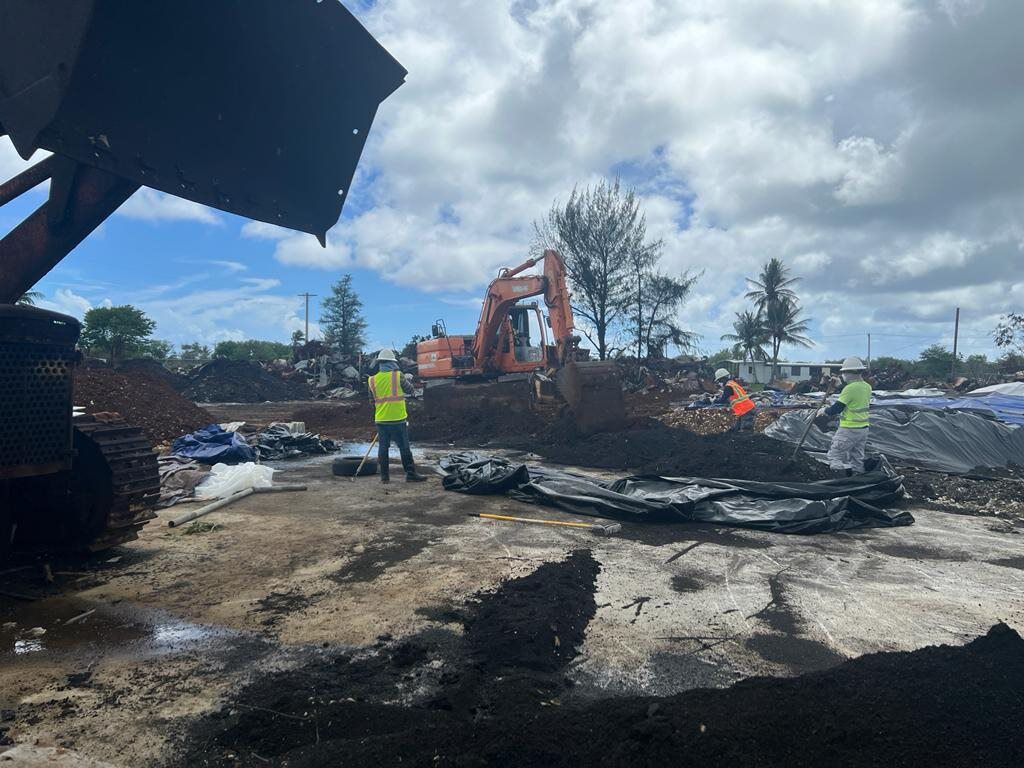 In this photo from early July, APEC personnel at the Super Typhoon Yutu waste and debris site on Tinian clean up piles of burnt solid waste at the site. Also pictured is large plastic sheeting which prevents contaminants from the burned materials from seeping into the soil.