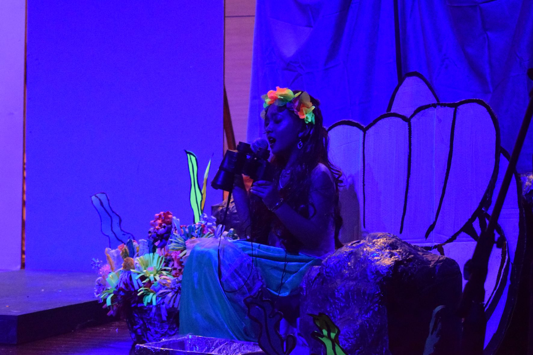 Ariel sings as she holds a pair of binoculars which she uses to watch the distant world.