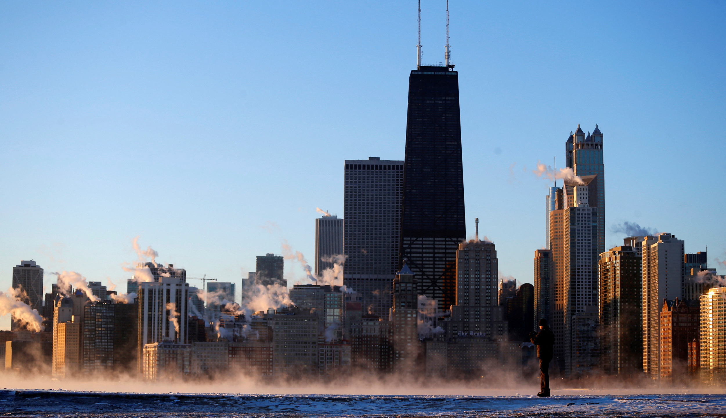 A man takes a picture against the Chicago skyline as the steam fog rises off Lake Michigan in Chicago, Illinois, Jan. 28, 2014.