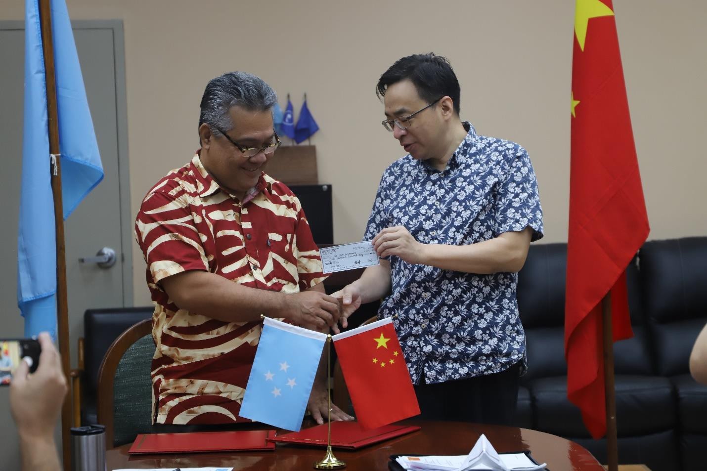Marcus H. Samo, secretary of the Department of Health & Social Affairs of the Federated States of Micronesia, and Huang Zheng, China’s ambassador to the FSM, pose for a handshake while the diplomat holds a check for $200,000 to assist the FSM in tackling Covid-19.