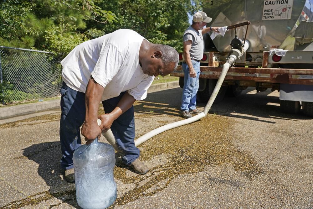 Ty Carter, right, and Benjamin Williams, with Garrett Enterprises, fill up a five-gallon jug for an area resident from a water tanker at Forest Hill High School in Jackson, Miss., Wednesday, Aug. 31, 2022. The tanker, is one of two placed strategically in the city to provide residents non-potable water.