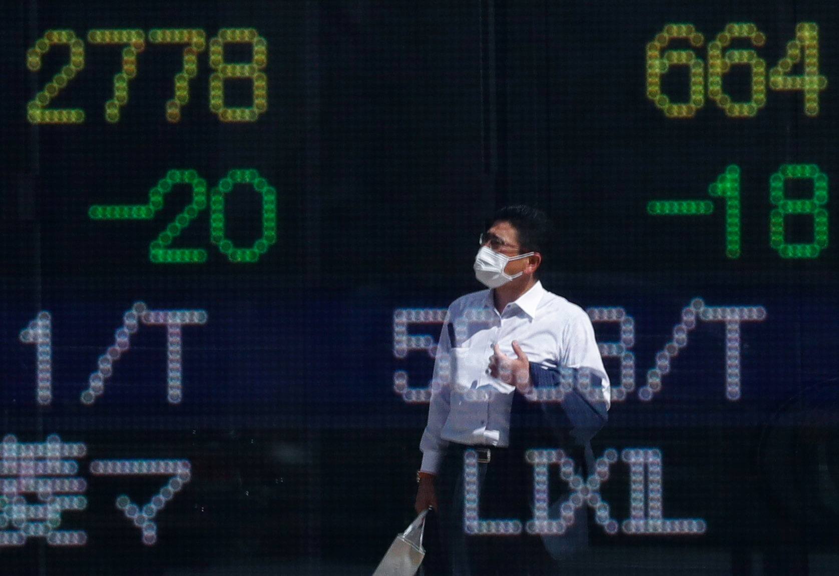 A man wearing a protective mask is reflected on an electronic board displaying stock prices outside a brokerage in Tokyo, Japan, Sept. 29, 2021.