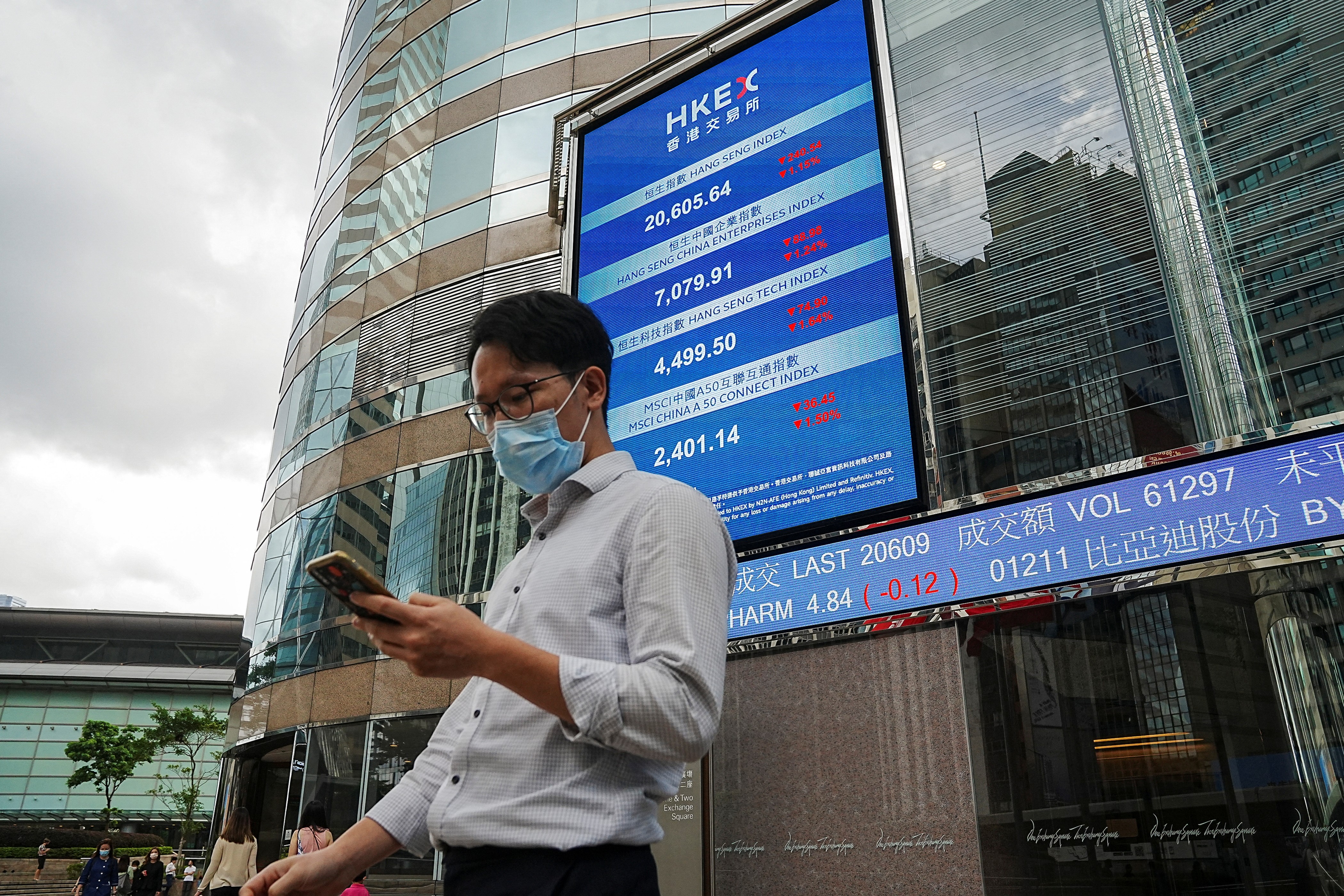 People walk past a screen displaying the Hang Seng stock index outside the Hong Kong Exchanges, in Hong Kong, July 19, 2022.