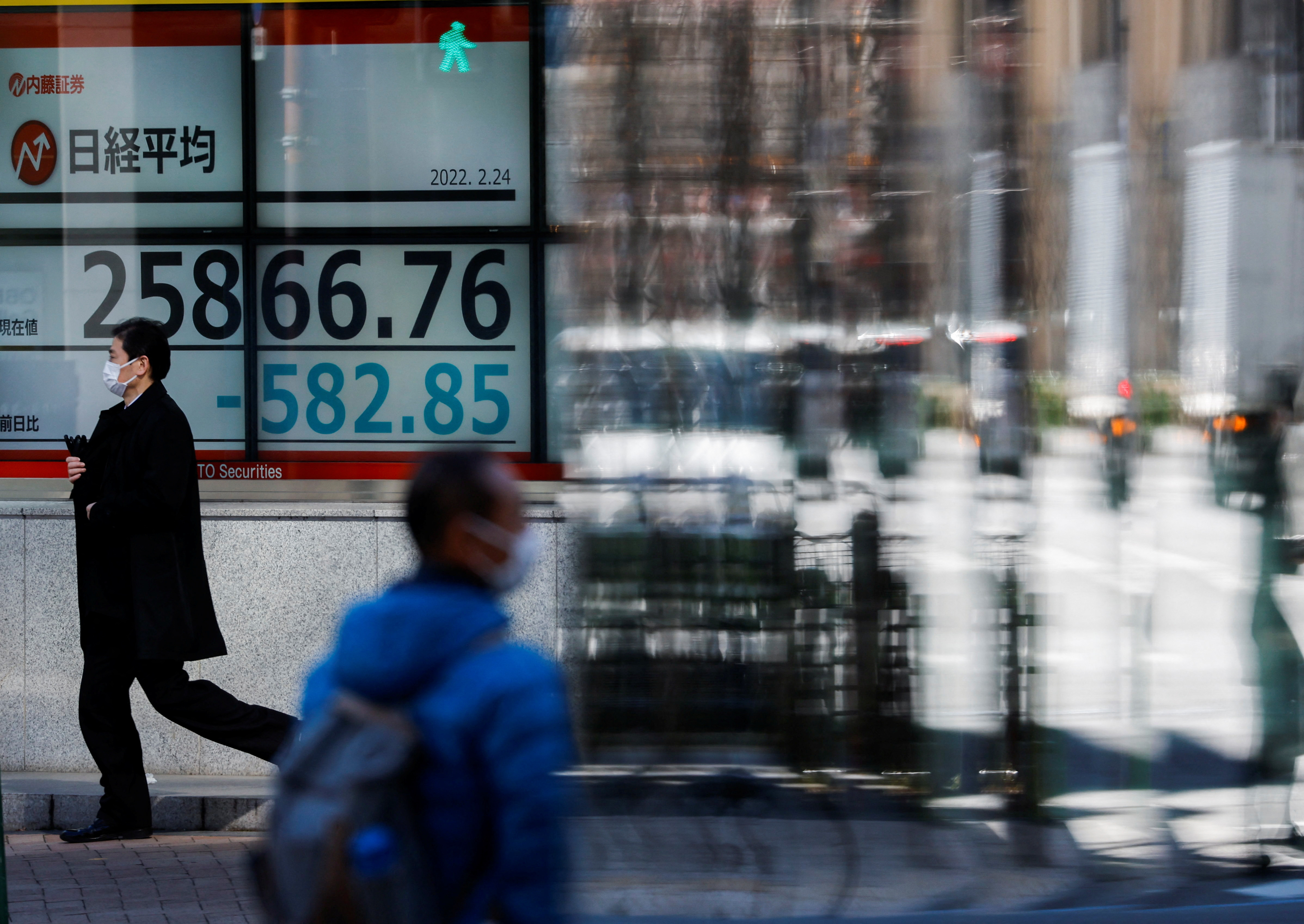 Passersby wearing protective face masks walk past a stock quotation board in Tokyo, Japan on Feb. 24, 2022.