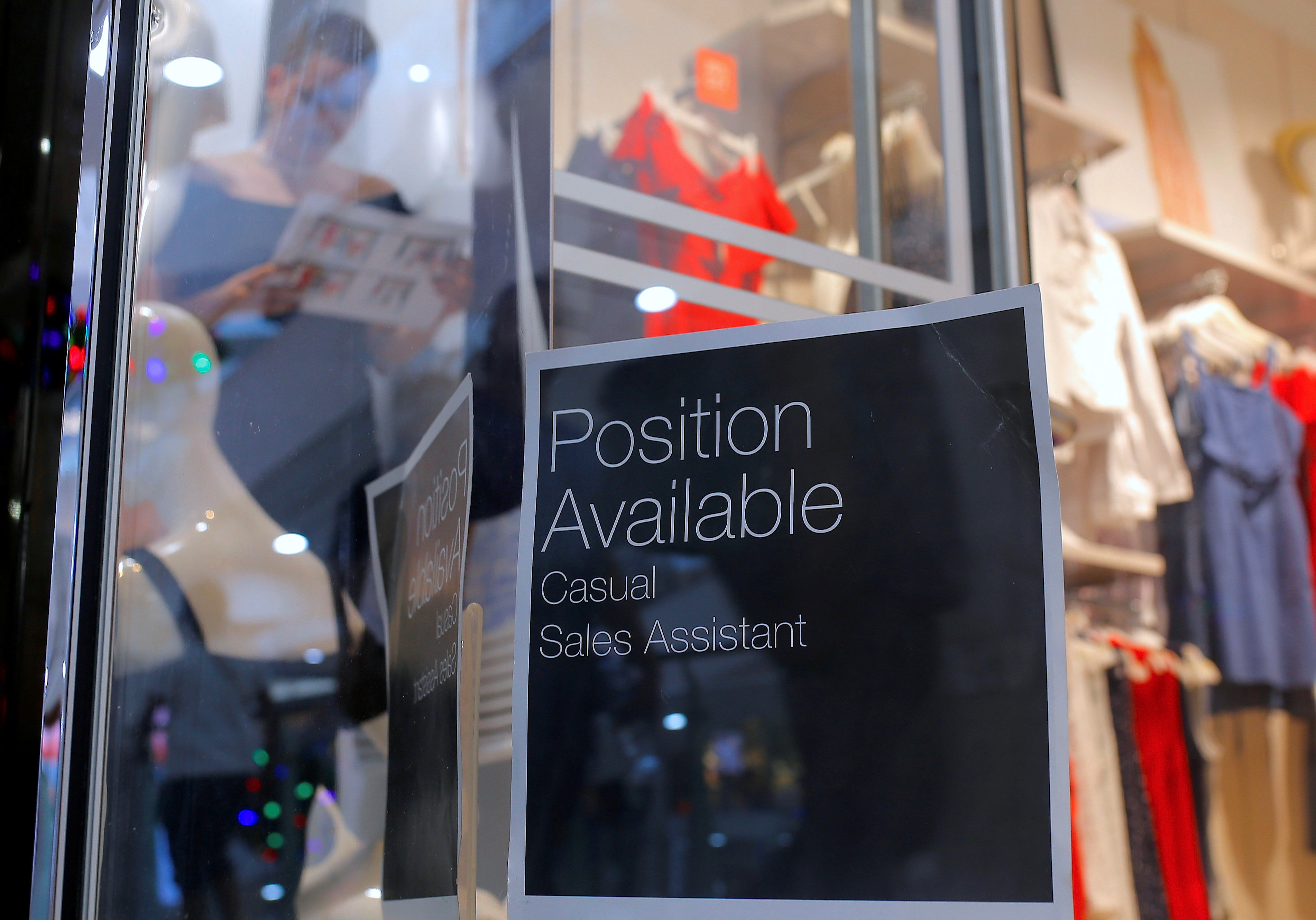 A sales assistant is seen through the window of a retail store displaying a job vacancy sign in central Sydney, Australia, Dec. 5, 2016.