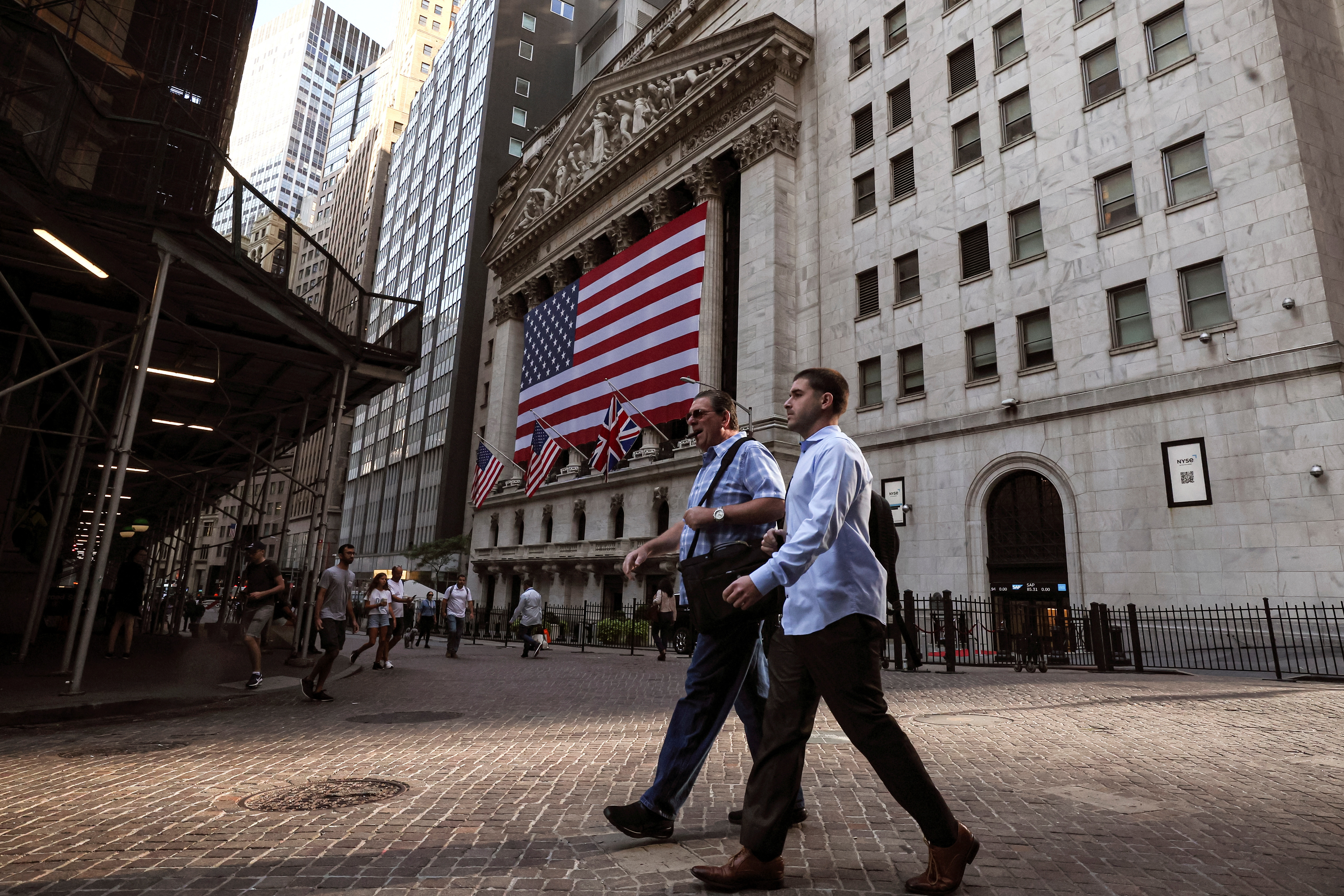 Morning commuters walk on Wall St. as the Union Jack flies at half staff outside the New York Stock Exchange in New York City, Sept. 9, 2022.