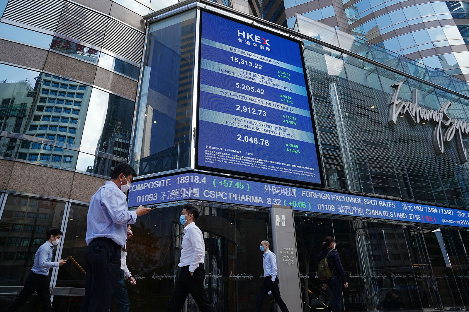 People walk past a screen displaying the Hang Seng stock index at Central district, in Hong Kong, China, Oct. 25, 2022.