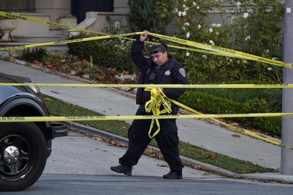 A police officer rolls out more yellow tape on the closed street below the home of Paul Pelosi, the husband of House Speaker Nancy Pelosi, in San Francisco, Friday, Oct. 28, 2022. Paul Pelosi was attacked and severely beaten with a hammer by an assailant who broke into their San Francisco home early Friday.