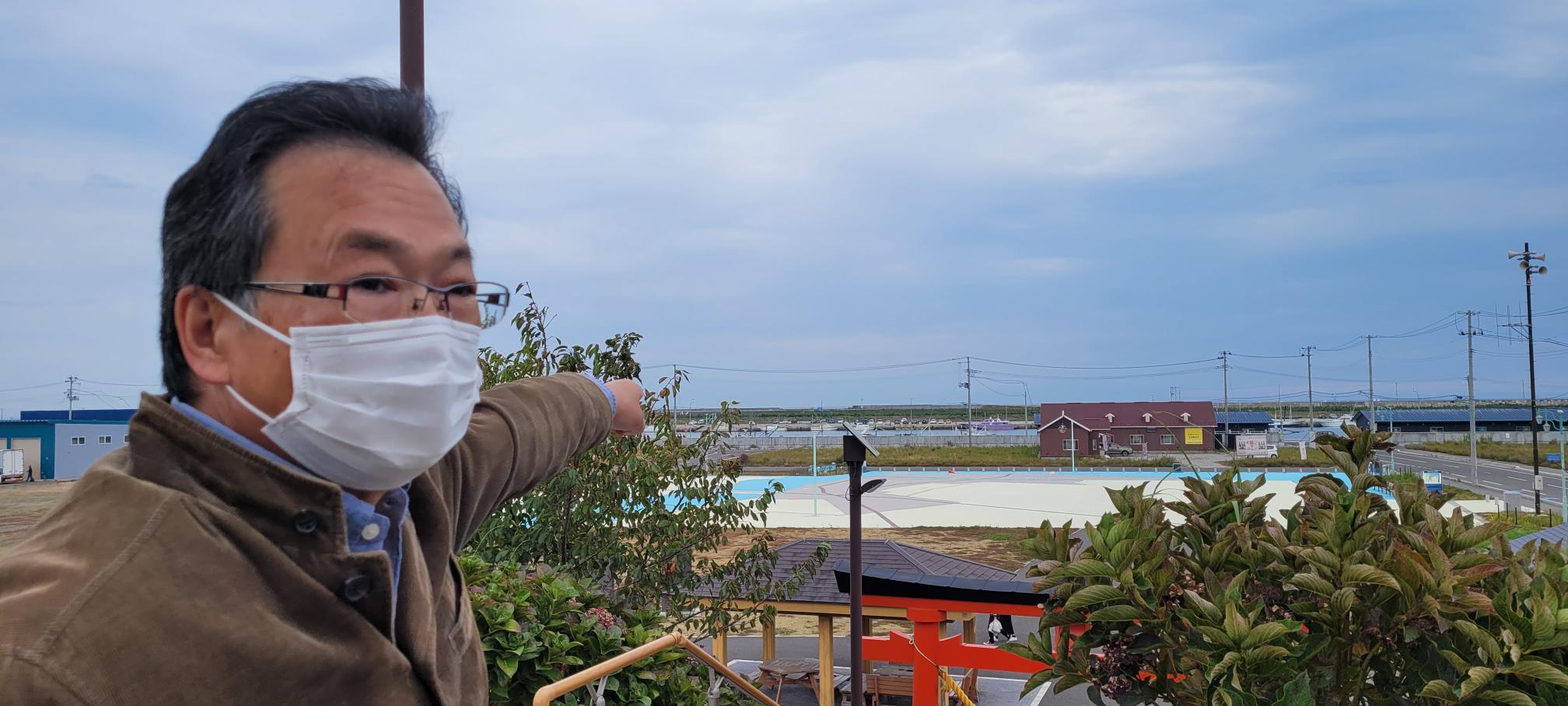 Naomitsu Kakui of the Association to Tell the Story of the Yuriage Disaster points to the east, where one of several tsunami waves tore through the district.