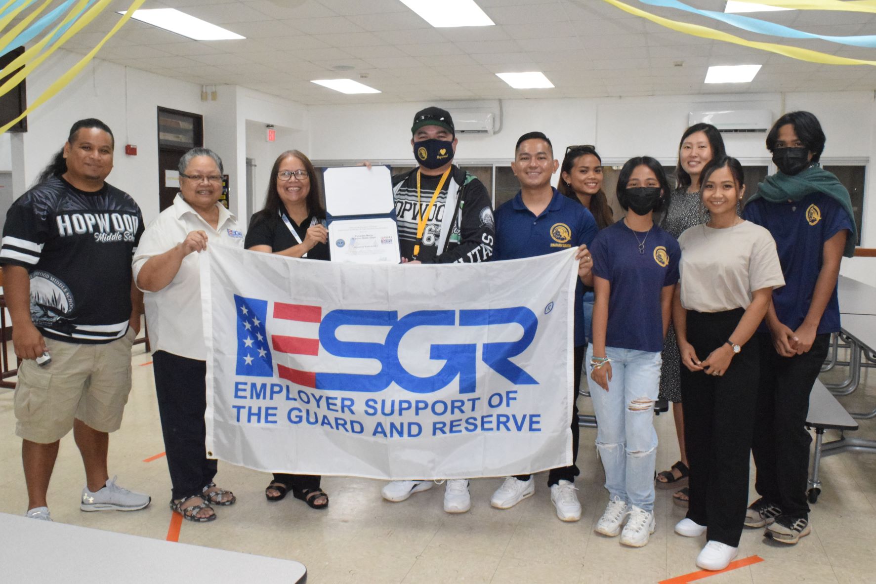 Hopwood Middle School Principal Victorino N. Borja, M.Ed., center, holds the Patriotic Employer Award as he poses for a photo with Employer Support of the Guard and Reserve Guam-CNMI Area Chair Rita A. Sablan, Ed.D., third left, Employer Outreach Coordinator Rose Igitol, second left, Hopwood teacher and U.S, Army Reserve Sgt. Jonathan Sugatan, sixth right, school staff and students in the Hopwood cafeteria on Tuesday.