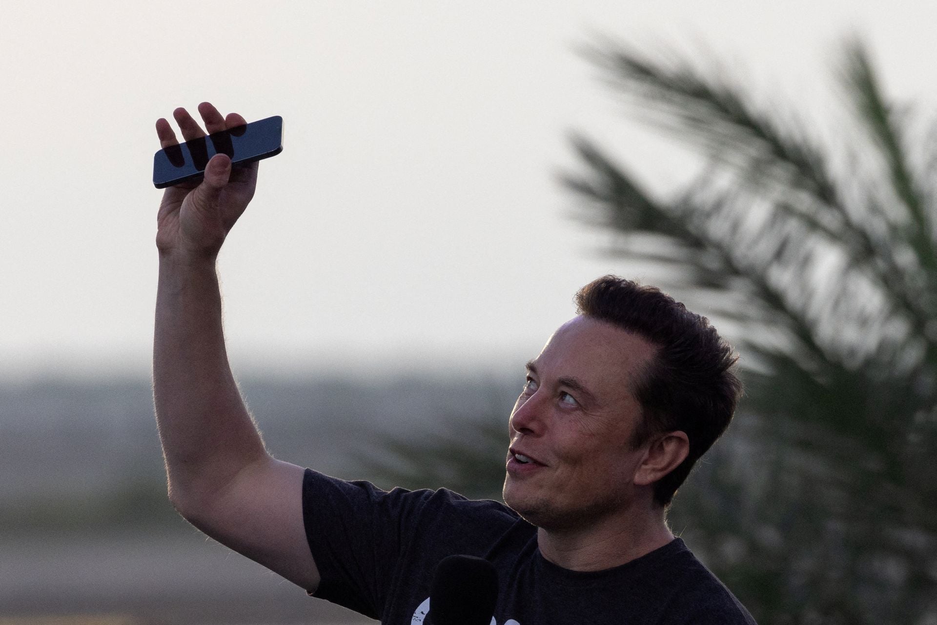 Elon Musk raises his phone towards the sky during a news conference at the SpaceX Starbase, in Brownsville, Texas, Aug. 25, 2022.