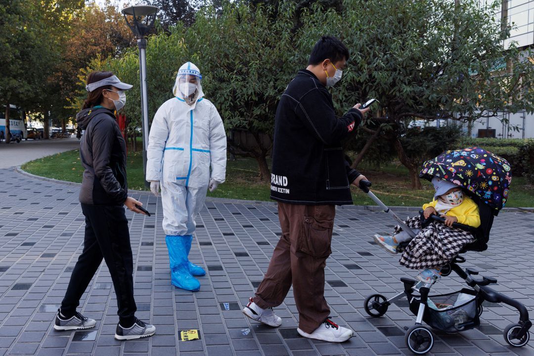 A pandemic prevention worker wears a protective suit as people line up to get swab tests at a testing booth as outbreaks of Covid-19 continue in Beijing, China, Nov. 3, 2022.