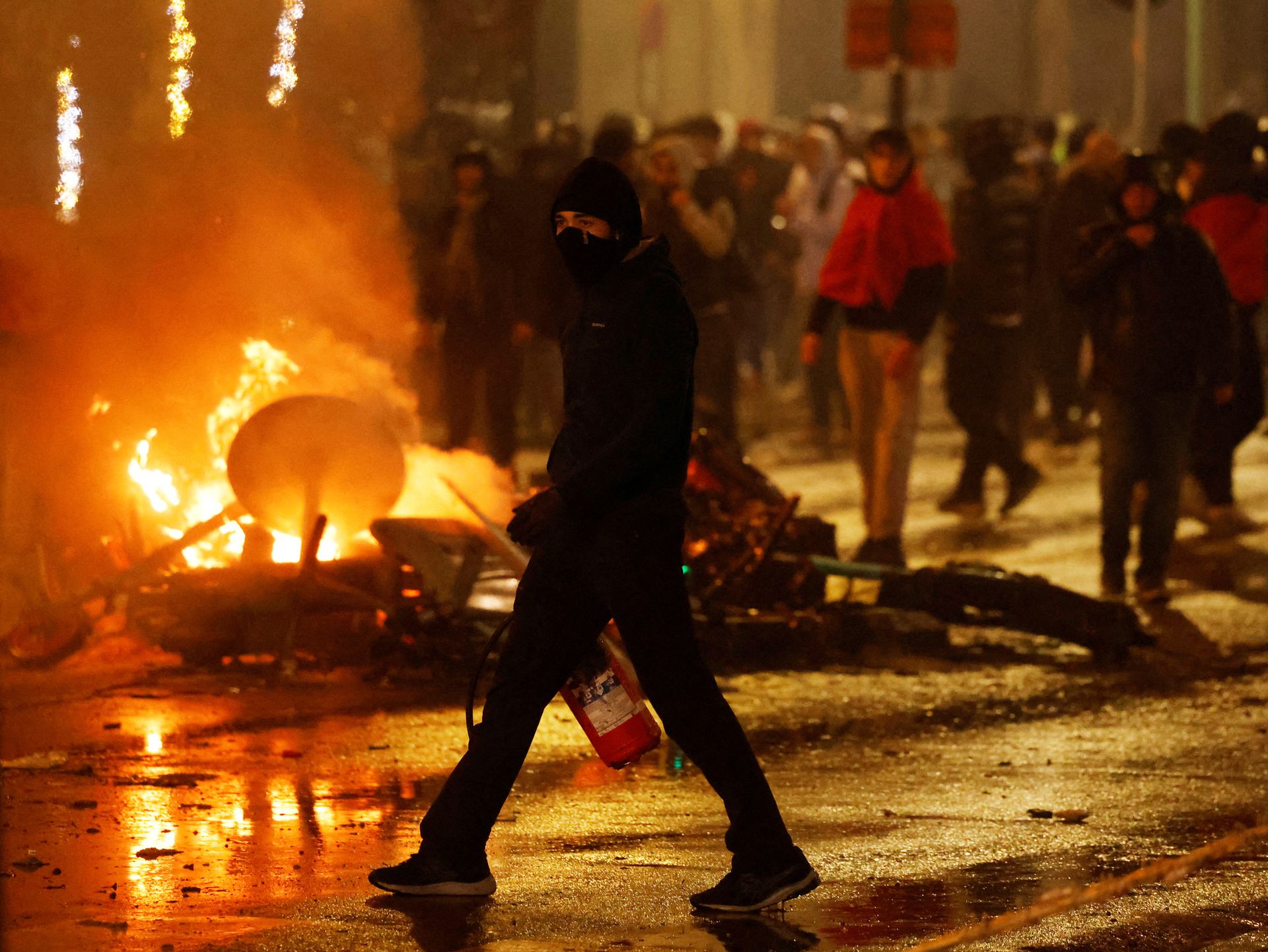 A man with his face covered and a fire extinguisher is seen during clashes after the World Cup match between Belgium and Morocco in Brussels, Belgium, Nov. 27, 2022