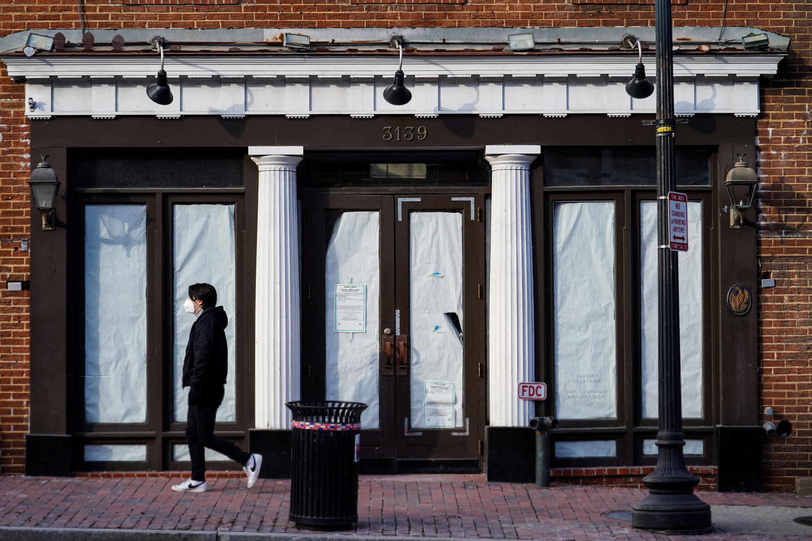 A person wearing a protective face mask walks past a closed business in the Georgetown neighborhood in Washington, D.C. Jan. 31, 2022. The coronavirus disease pandemic has shuttered many businesses in the once bustling shopping district.