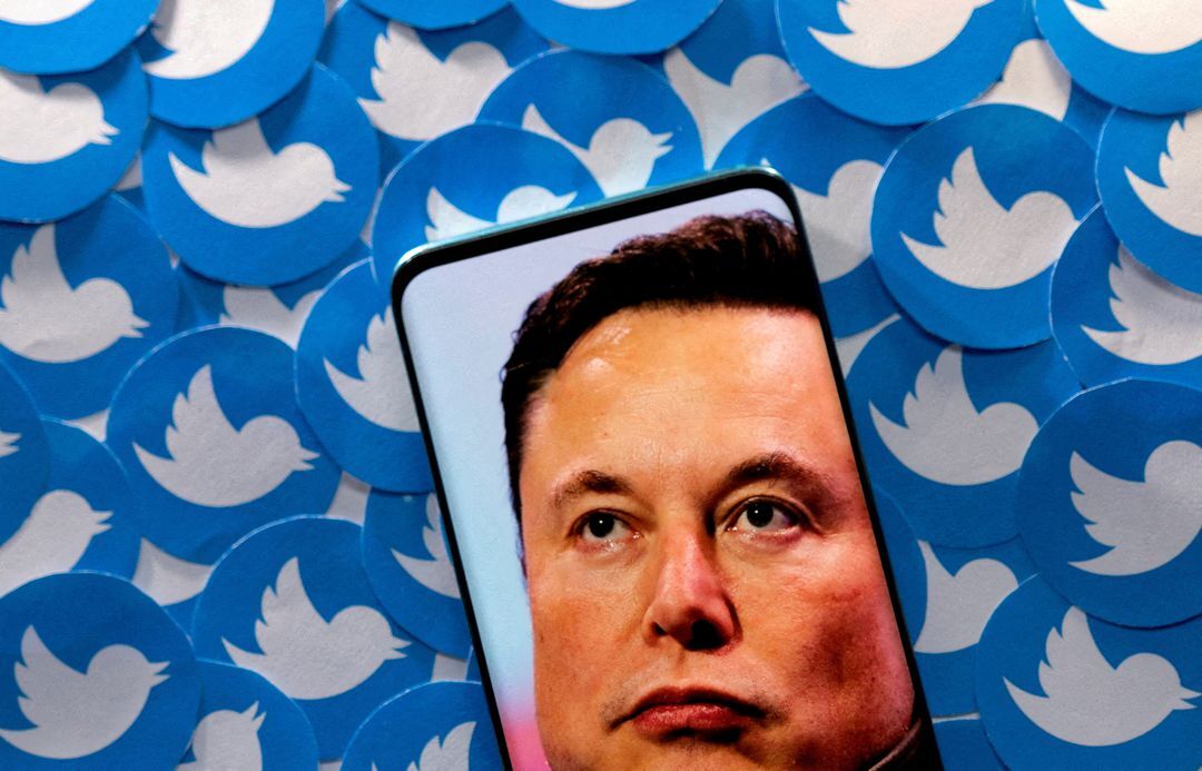 An image of Elon Musk is seen on a smartphone placed on printed Twitter logos in this picture illustration taken on April 28, 2022.