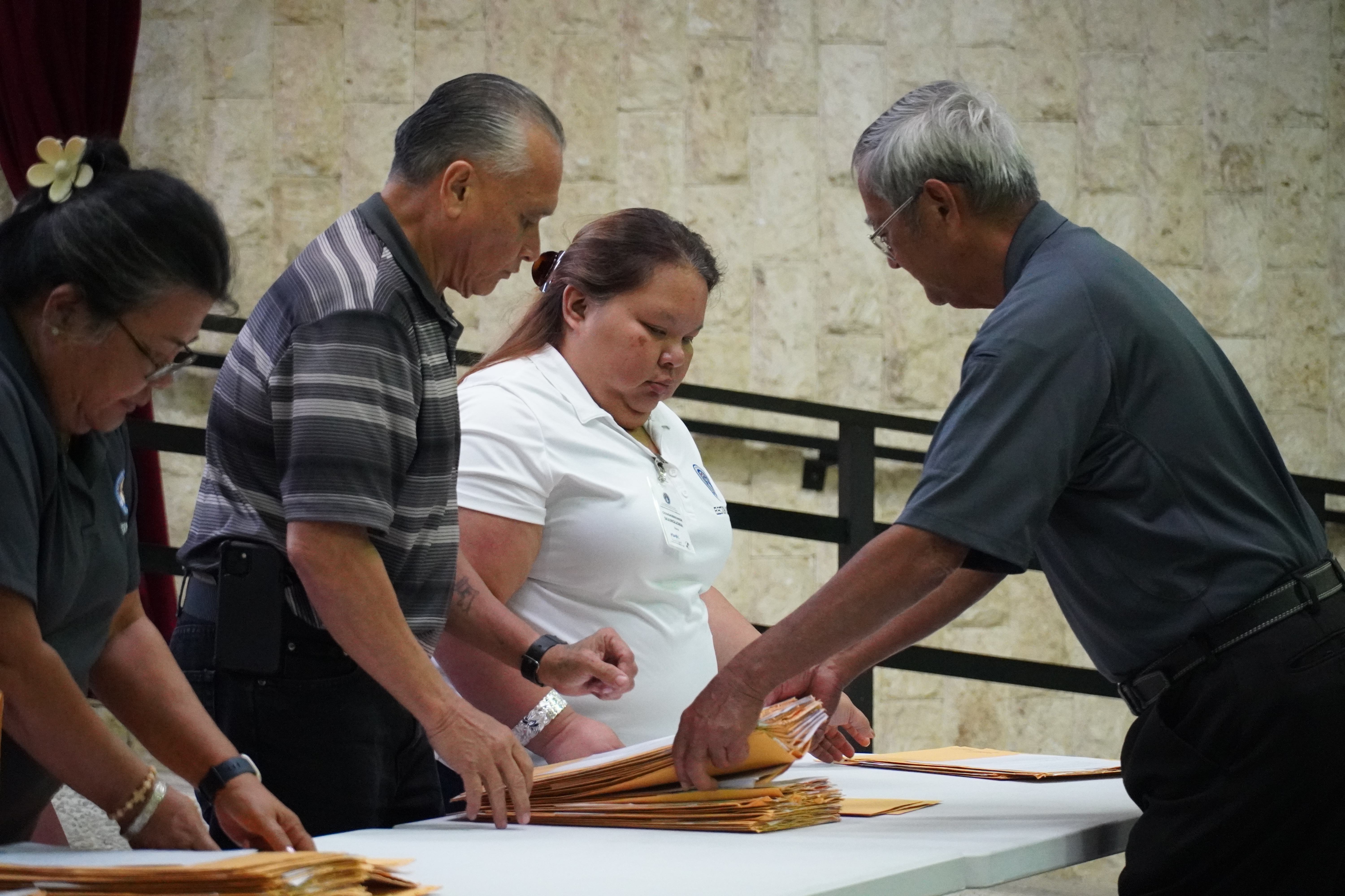 Election board chair Jesus I. Sablan hands stacks of absentee ballots to commissioners John Diego Attao and Lelanie I. Manglona.